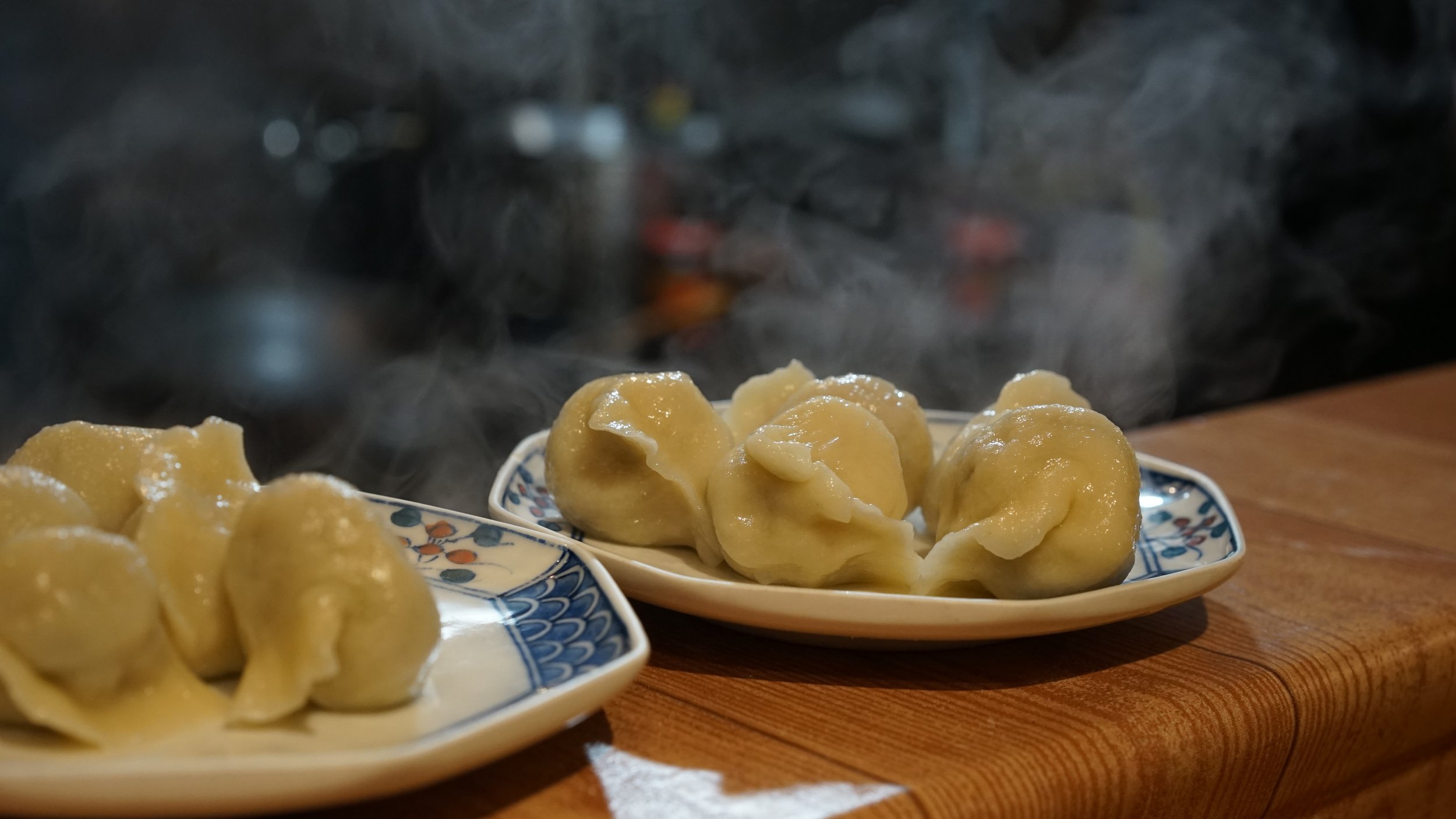 Steaming Tibetan dumplings on decorative plates placed on a wooden surface.