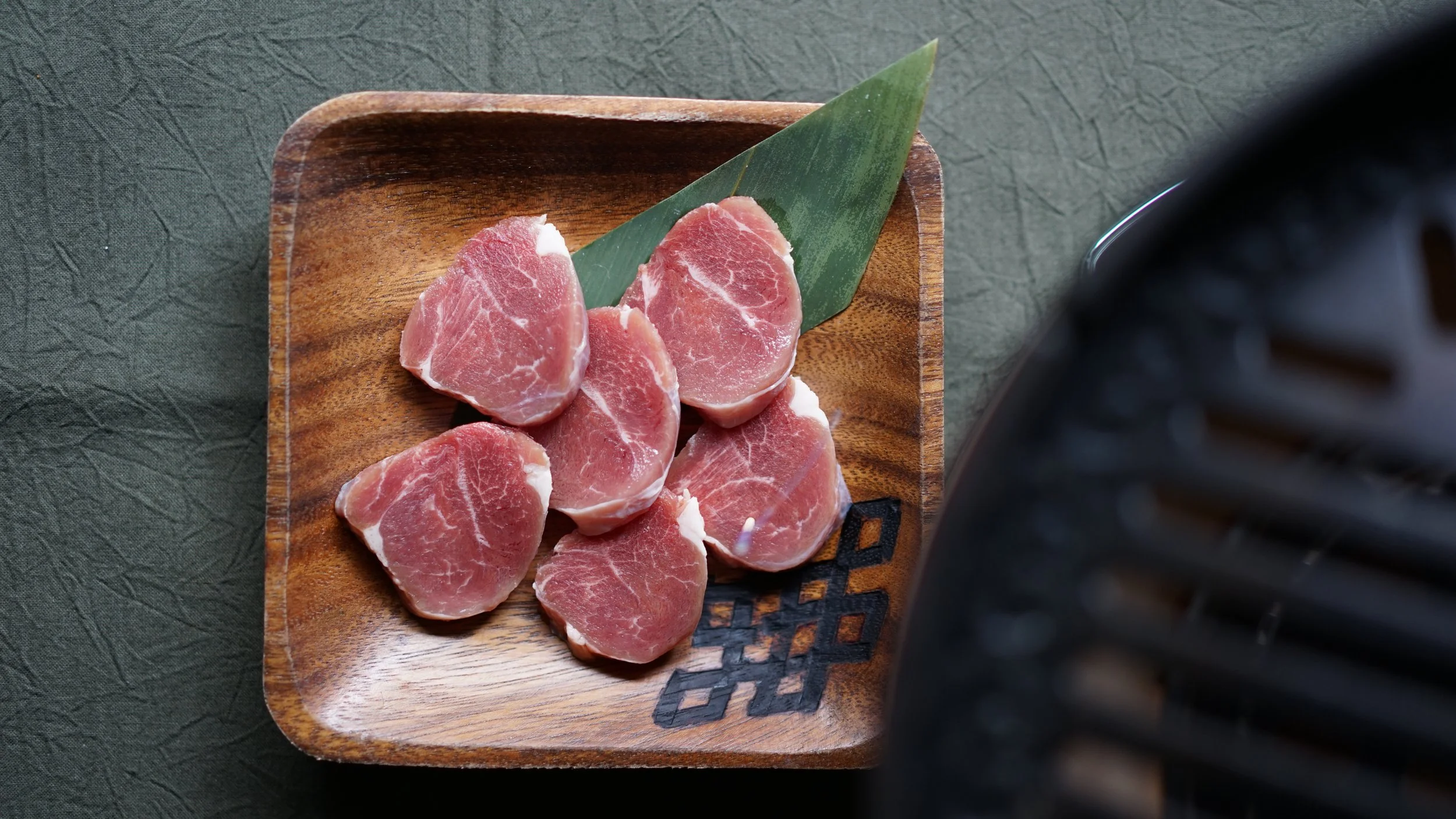 Raw slices of prosciutto on a wooden plate with a green leaf for presentation