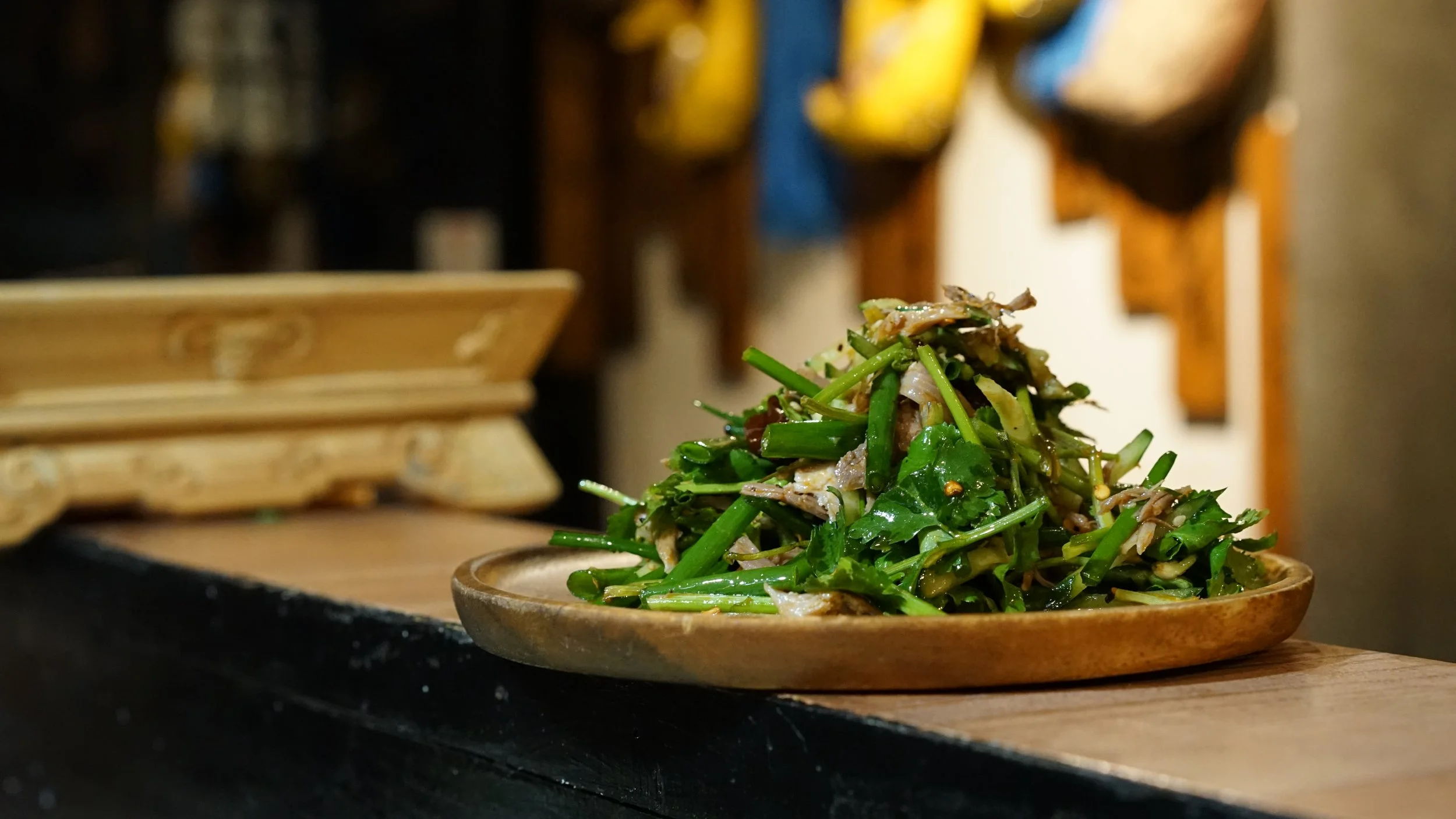 A plate of green vegetable stir-fry on a wooden table with blurred background.
