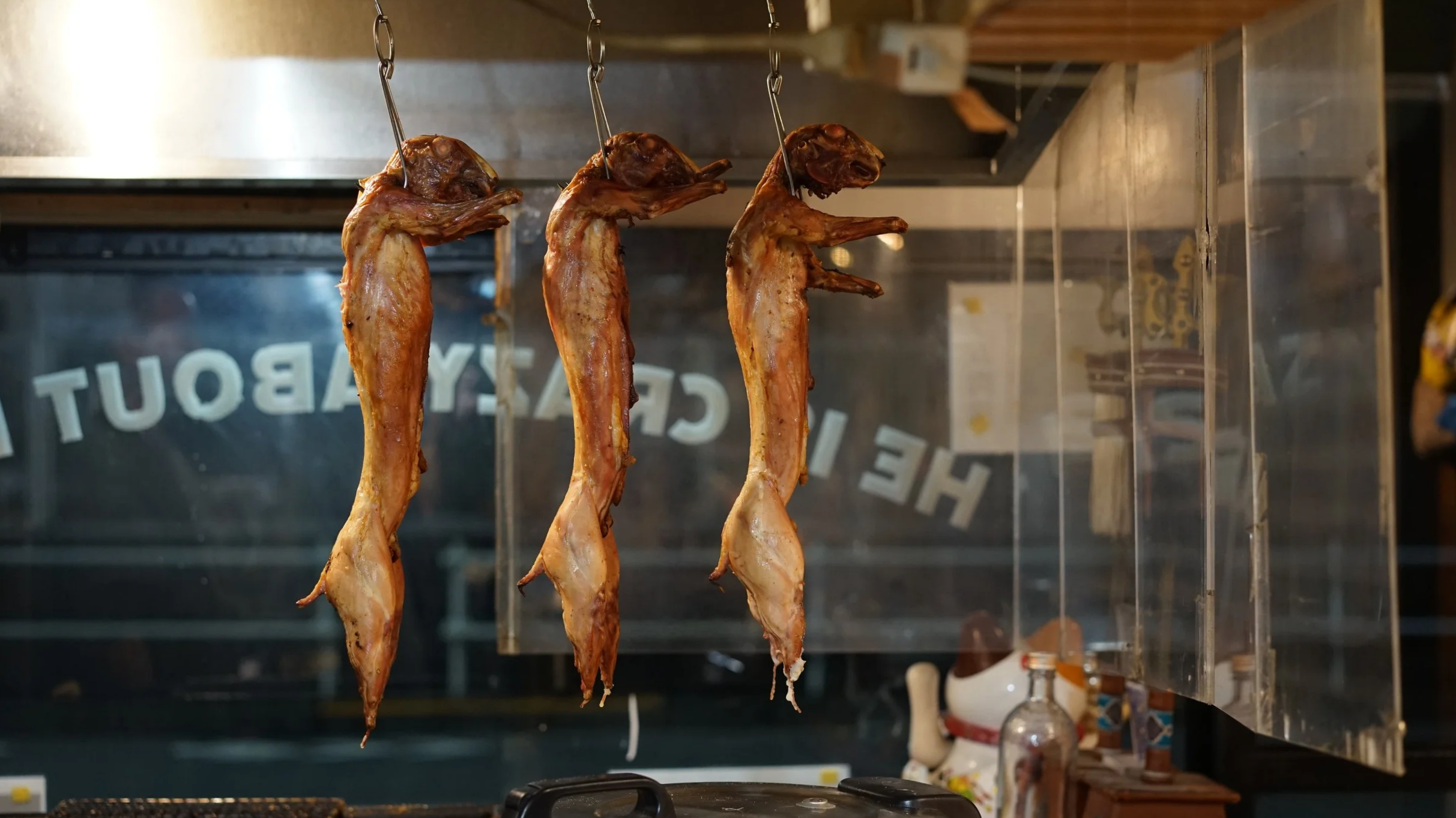 Three smoked fish hanging from hooks in a kitchen or restaurant setting.
