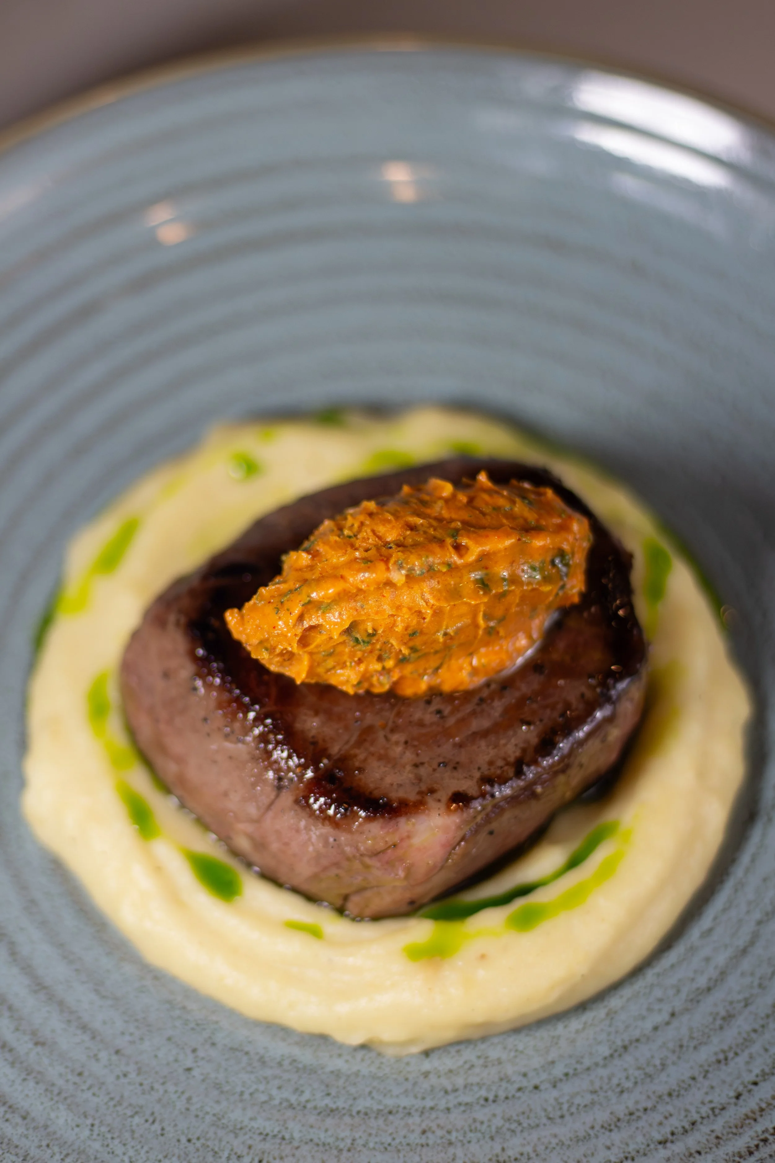 Filete de carne de res con una porción de puré y una salsa de color claro en el plato.