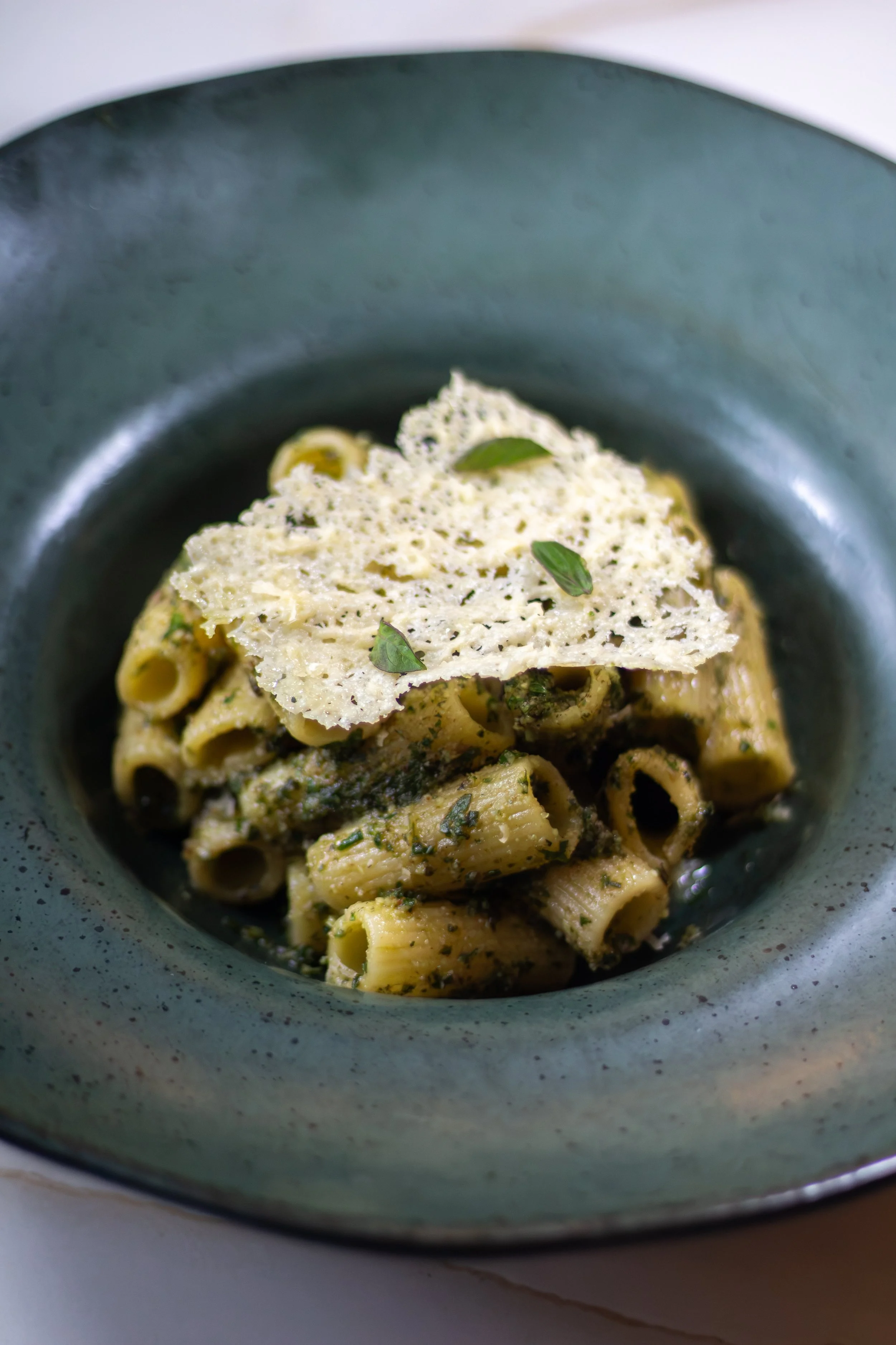 Plato de pasta con salsa y queso rallado, decorado con hojas de perejil, en un plato azul.