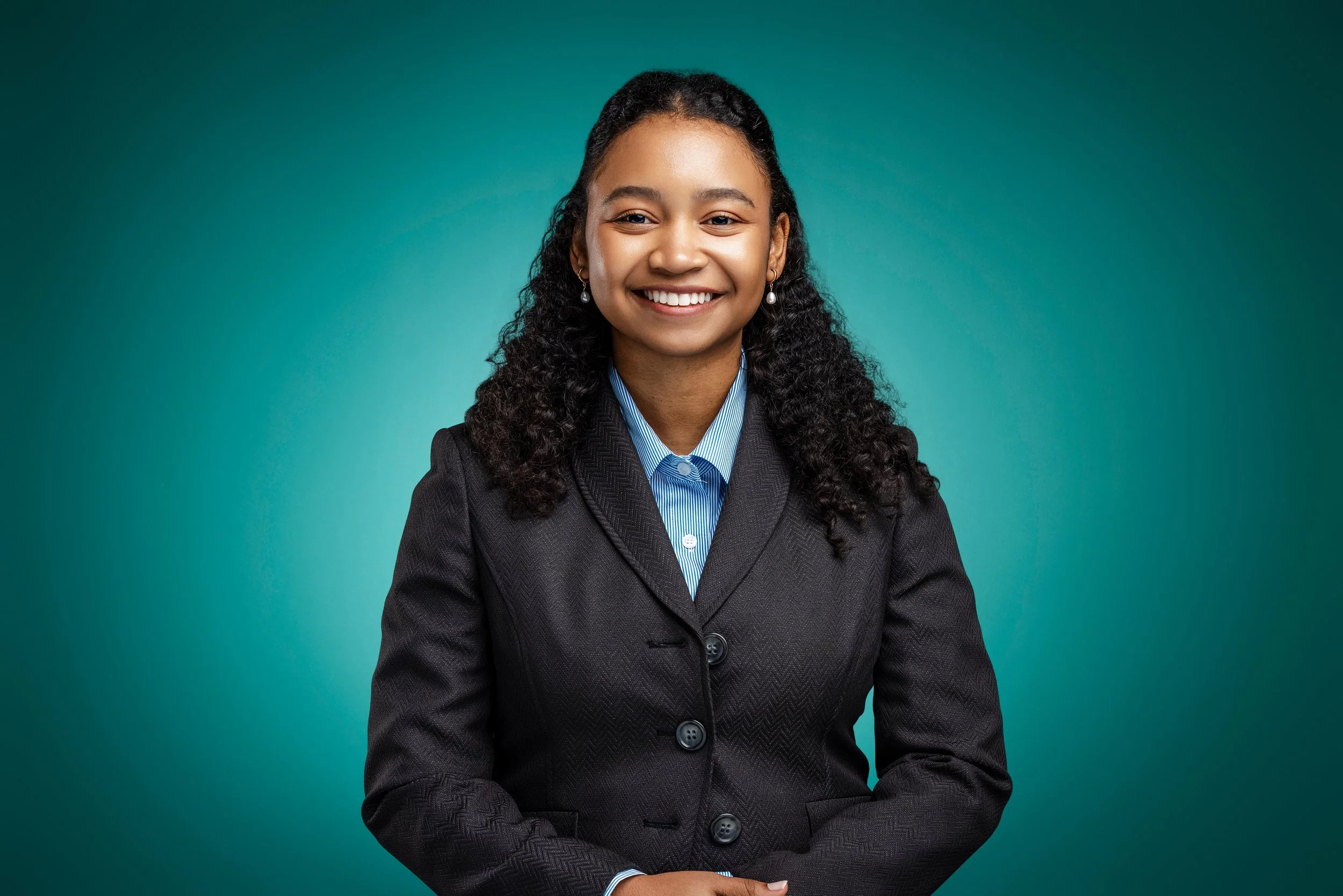 A smiling young woman in a business suit posing against a teal background.
