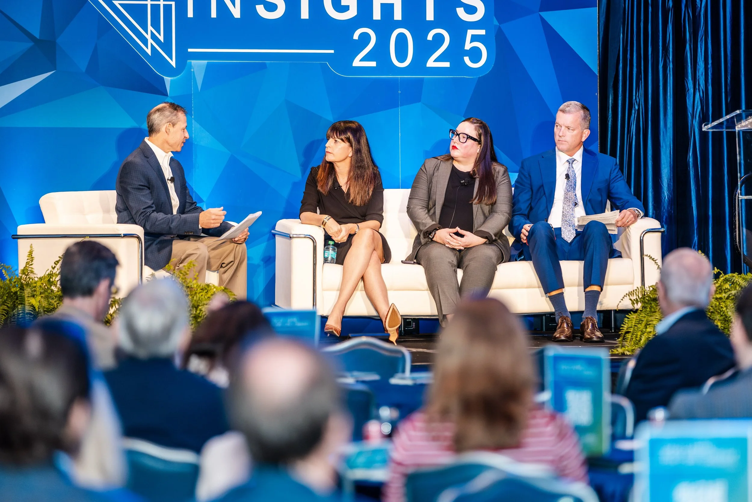 Four people on stage participating in a panel discussion at a conference, with an audience in the foreground.