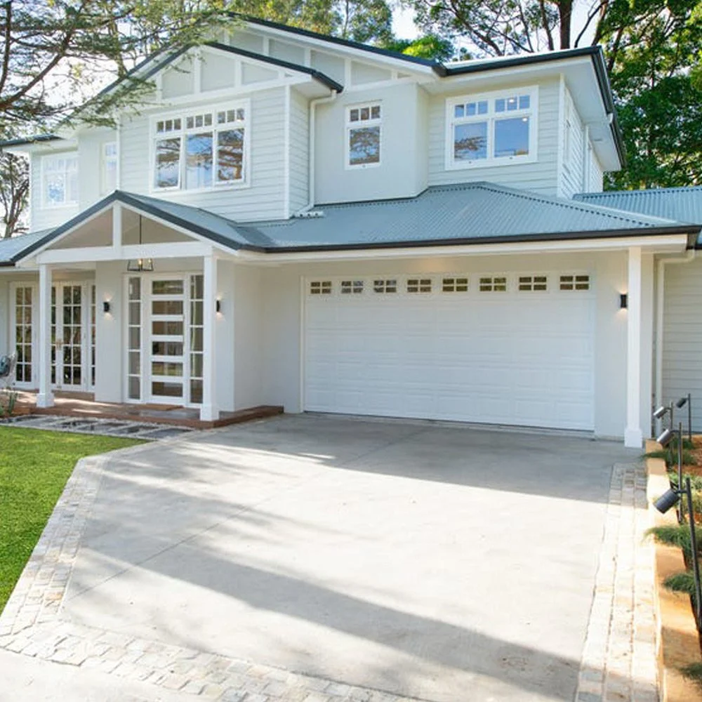 A modern two-story white house with a garage, front porch, and a paved driveway, surrounded by green grass and trees.