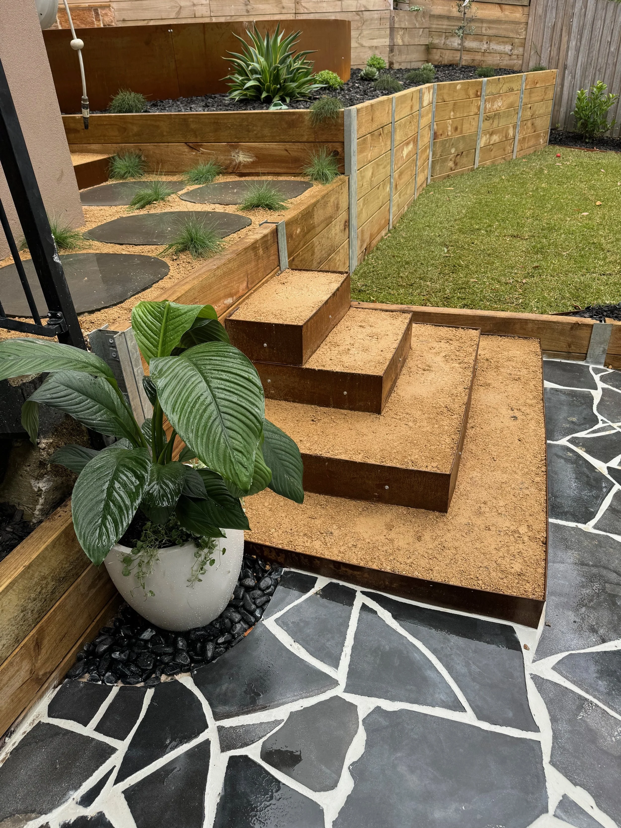 Backyard garden with deco stairs, potted plant, grassy lawn, ornamental plants, and decorative stone pathway.