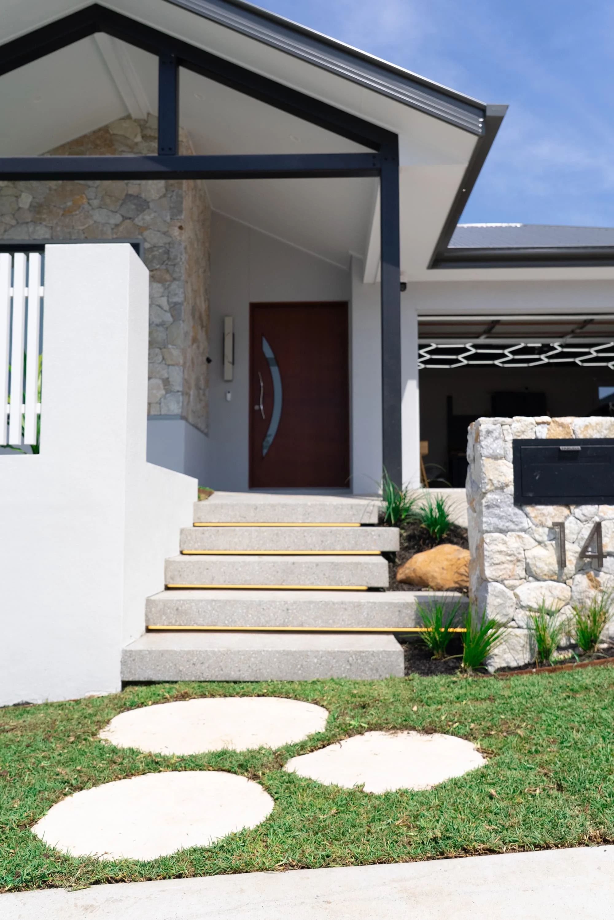 Modern house entrance with stairs, stone wall, and a wooden door under a sloped roof.