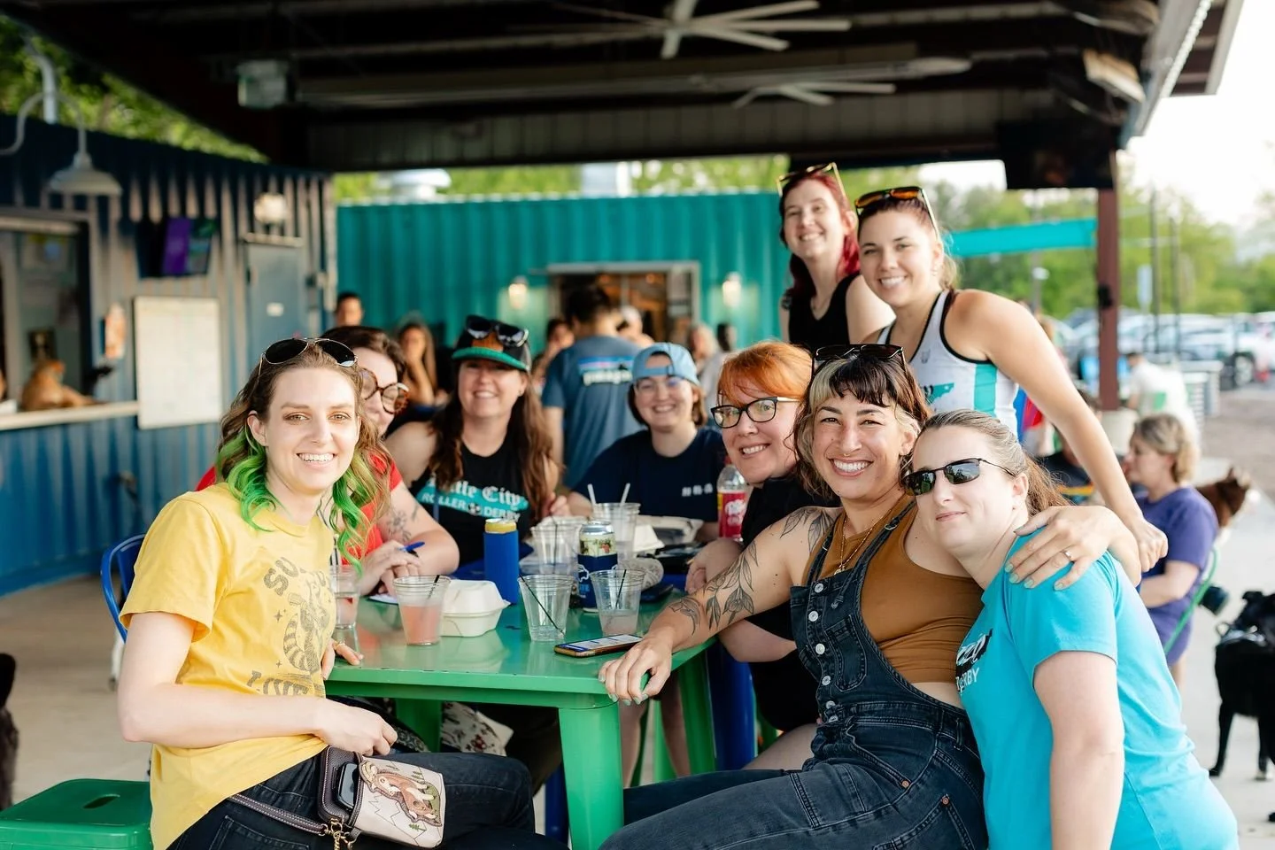 Dog owners socializing with their dogs off-leash in the park area at Off Leash Social enjoying drinks and food
