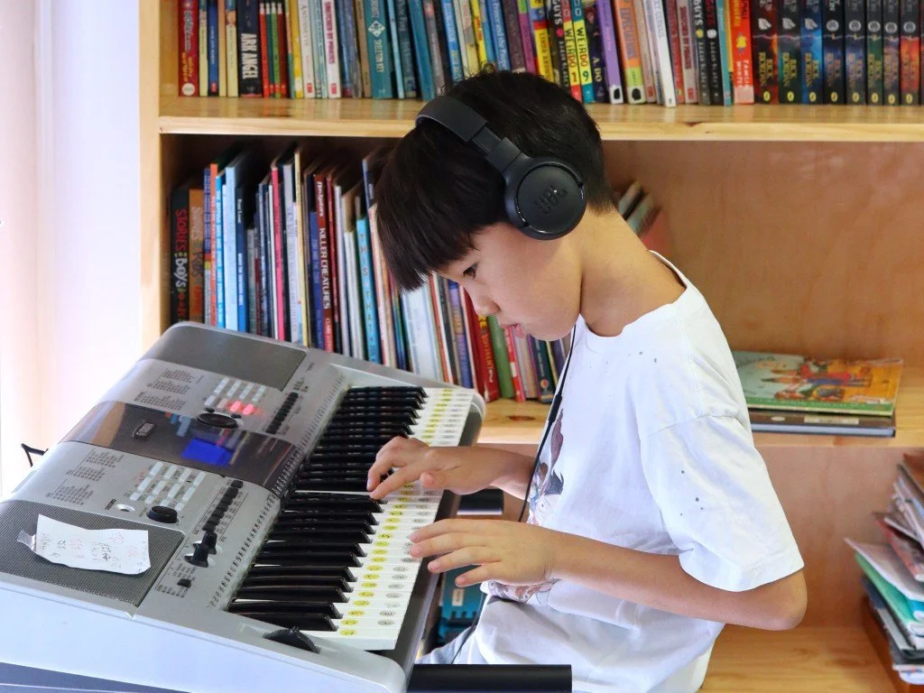 An Upper Primary student playing a keyboard with a bookshelf in the background.