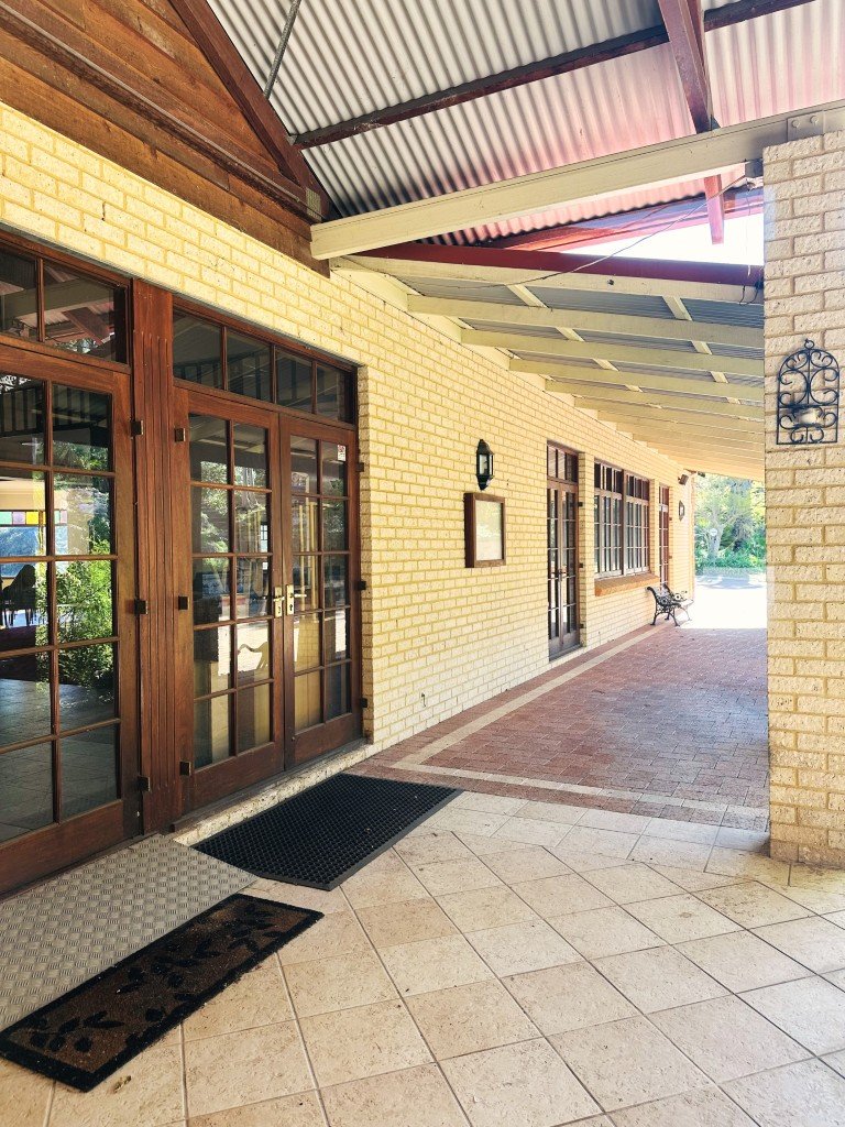 Covered outdoor corridor with a bench, brick walls, and wooden framed glass doors. This is the accessible entrance.
