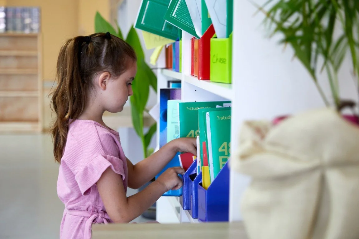 A primary school aged student is putting away books on a book shelf at out Port Kennedy campus