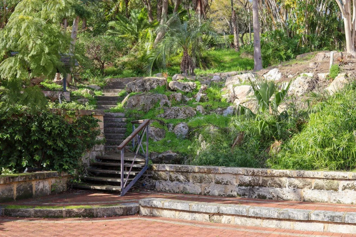 The landscaped garden area with stone steps, lush green plants, trees, and bushes, behind the function centre.