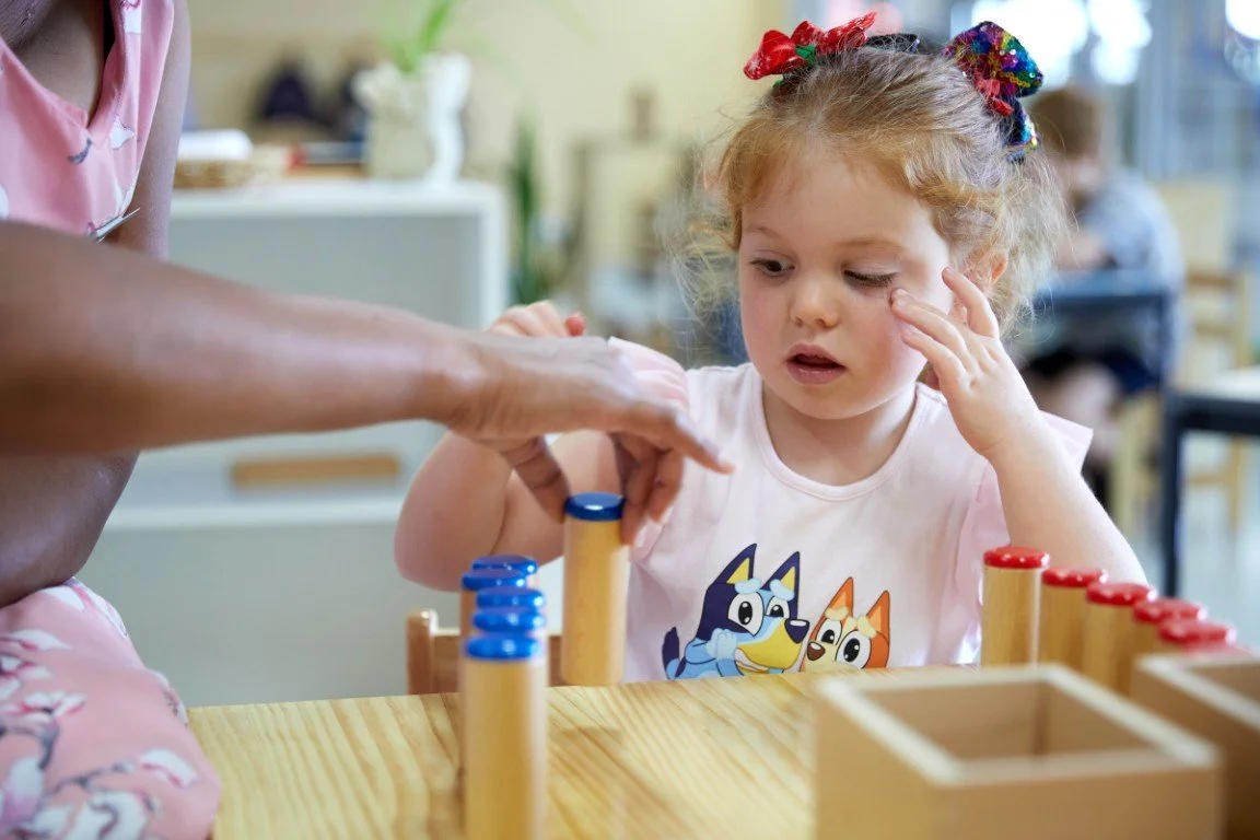 A pre-kindy toddler working with Montessori materials with the assistance of a teacher