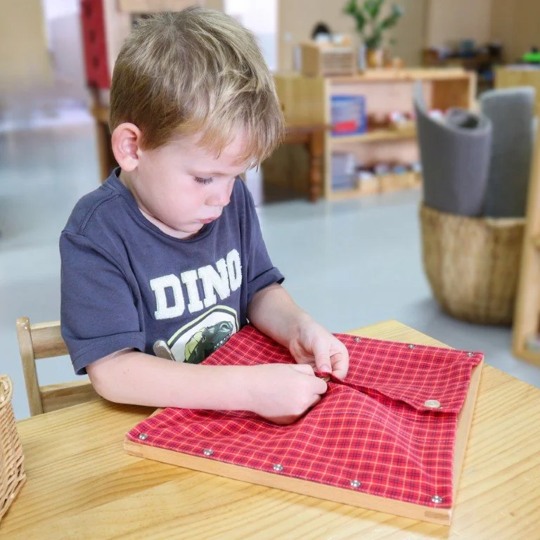 A Kindergarten student is working on the Montessori button frame
