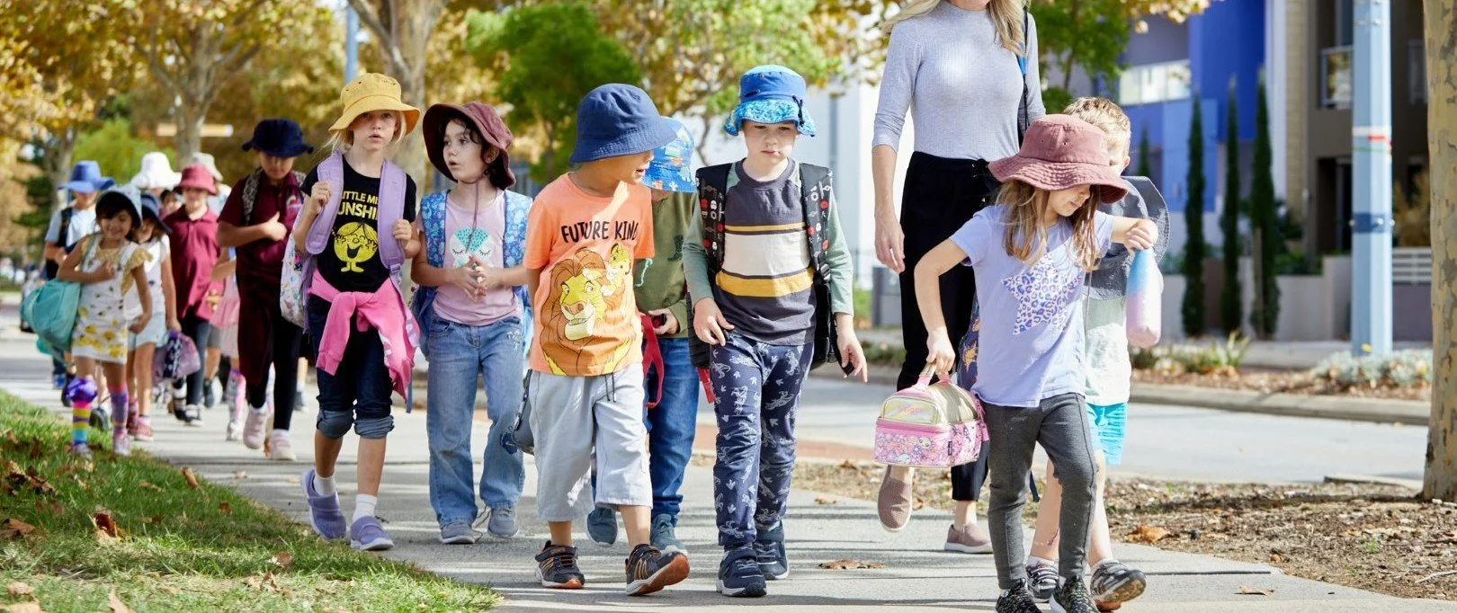 A group of children walking on a sidewalk, on their way to or from school, accompanied by an adult.