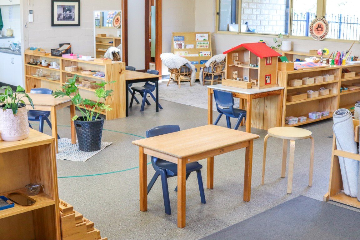 Interior of a child-friendly Montessori classroom with wooden shelves, tables, chairs, and various educational materials and toys.