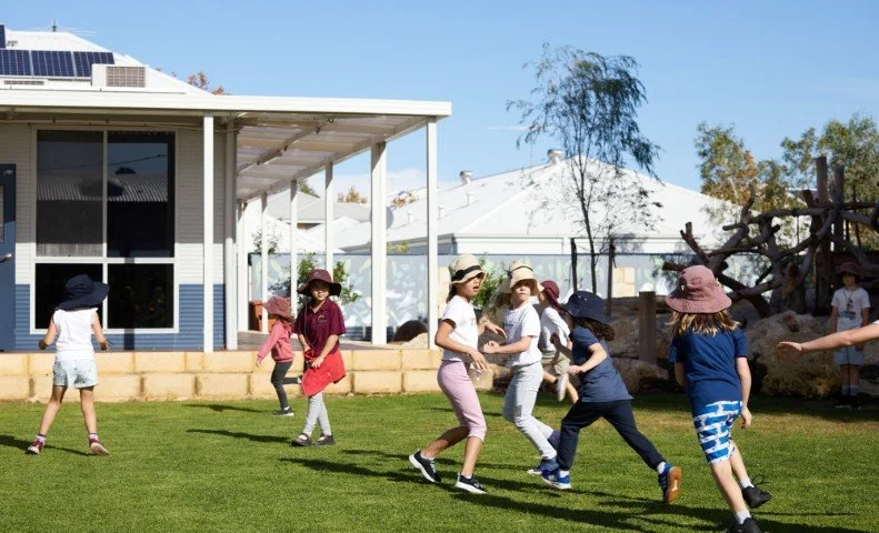 Children playing on a grassy yard in front of a primary school building