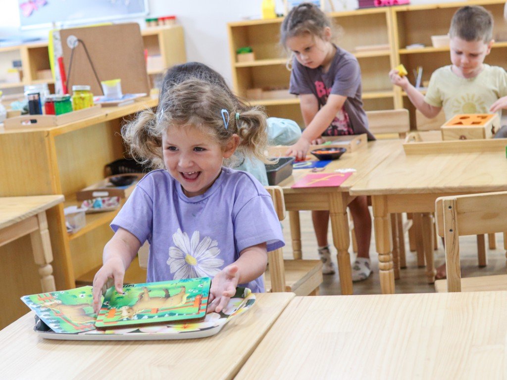 Children in an Early Learning classroom engaging in Montessori activities, with girl smiling.