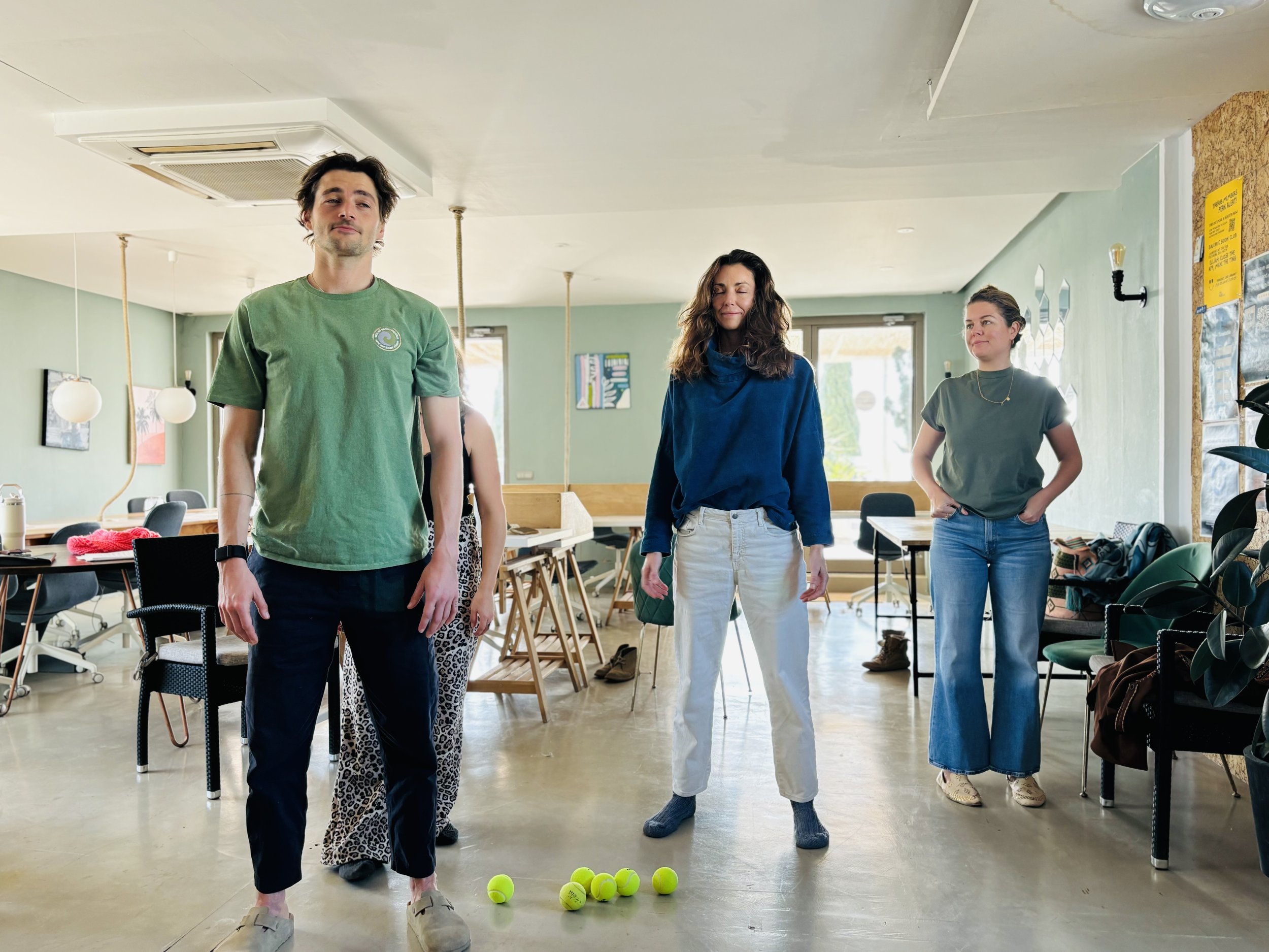 Varias personas en una sala jugando o participando en una actividad con pelotas de tenis en el suelo.