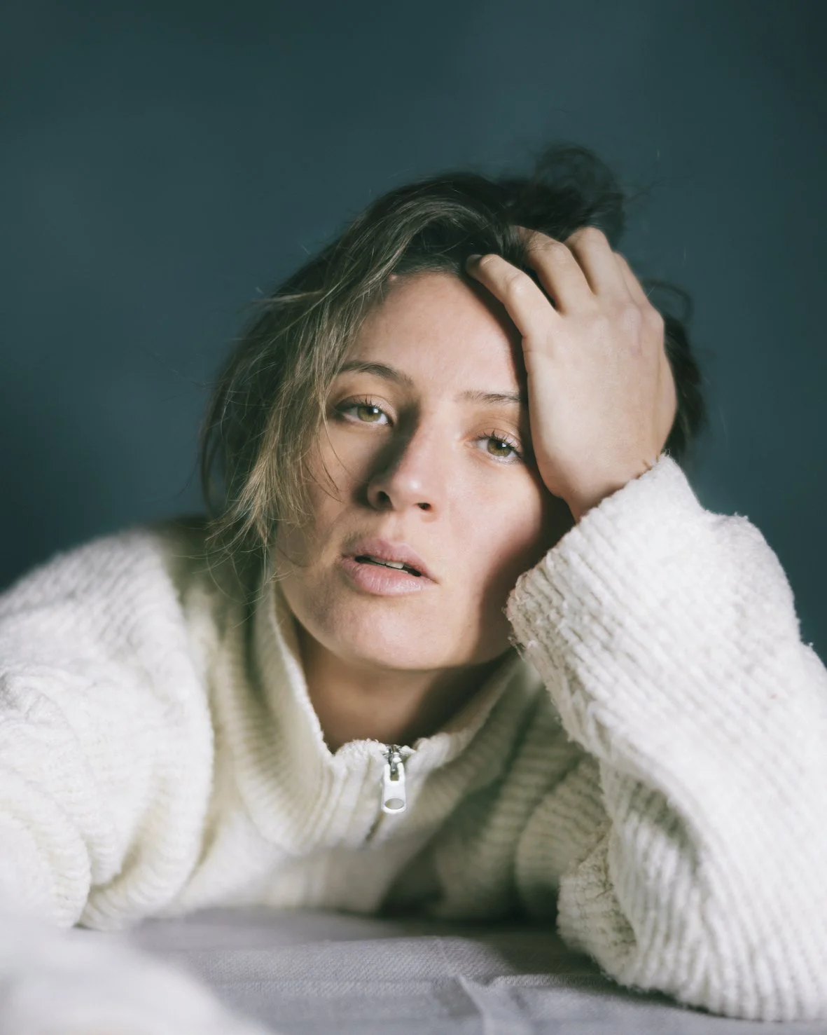 Mujer con expresión de fatiga o estrés, apoyando la cabeza con una mano, con fondo oscuro y luz suave