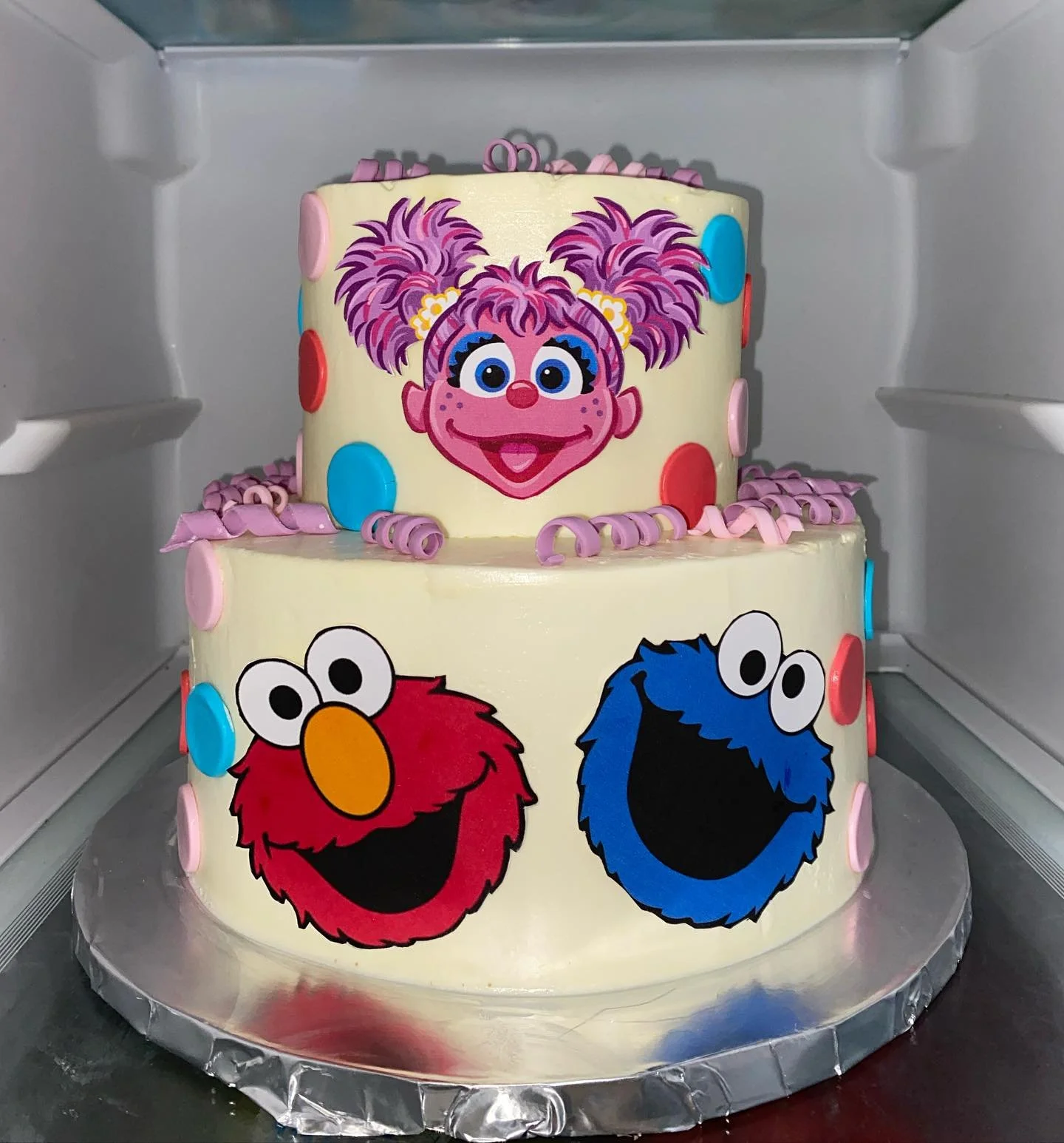 Two-tier birthday cake decorated with colorful Sesame Street characters, including Abby Cadabby on the top tier and Elmo and Cookie Monster on the bottom tier.