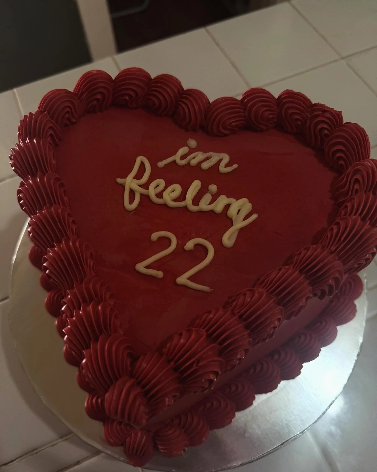 Heart-shaped cake with red frosting and decorative piping around the edges, with white icing writing that says "I'm feeling 22."