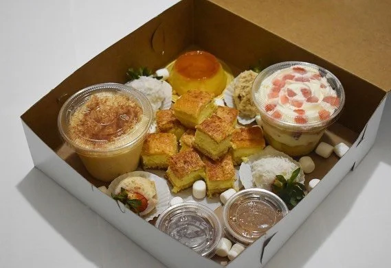Assorted desserts in a white box, including mini cakes, pudding, whipped cream, strawberries, and candy