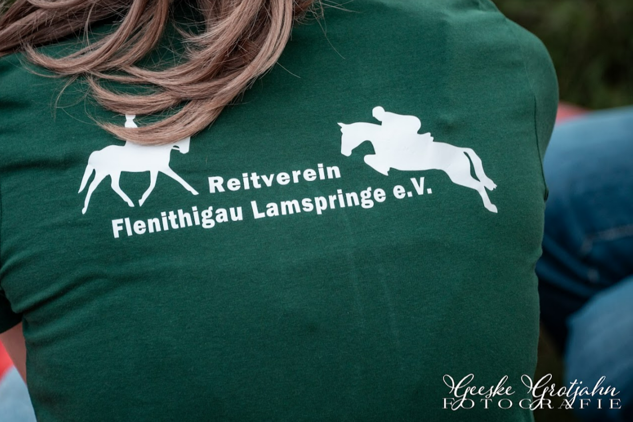Ein grünes T-Shirt mit weißen Silhouetten von einem Springreiter und einem Pferd. Darauf steht: 'Reitverein Flenithigau Lamspringe e.V.'.