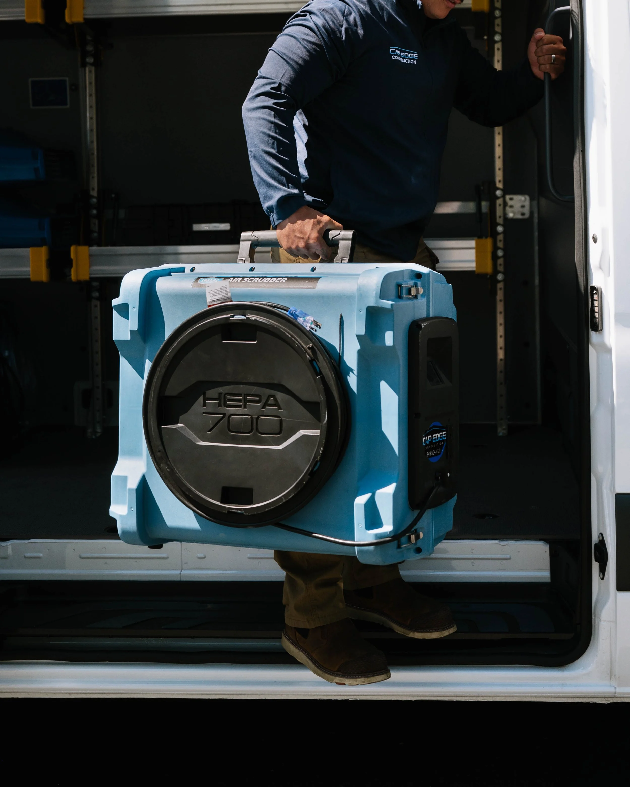 Three technicians working in a room with portable air conditioning units, a large window with a picture of bananas hanging from a string, and an air conditioning unit mounted on the wall.
