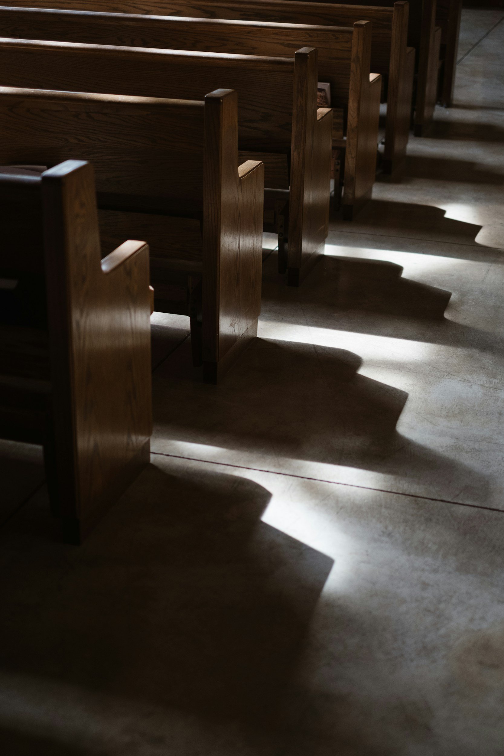 Rows of wooden pews in a church with sunlight casting shadows on the floor.