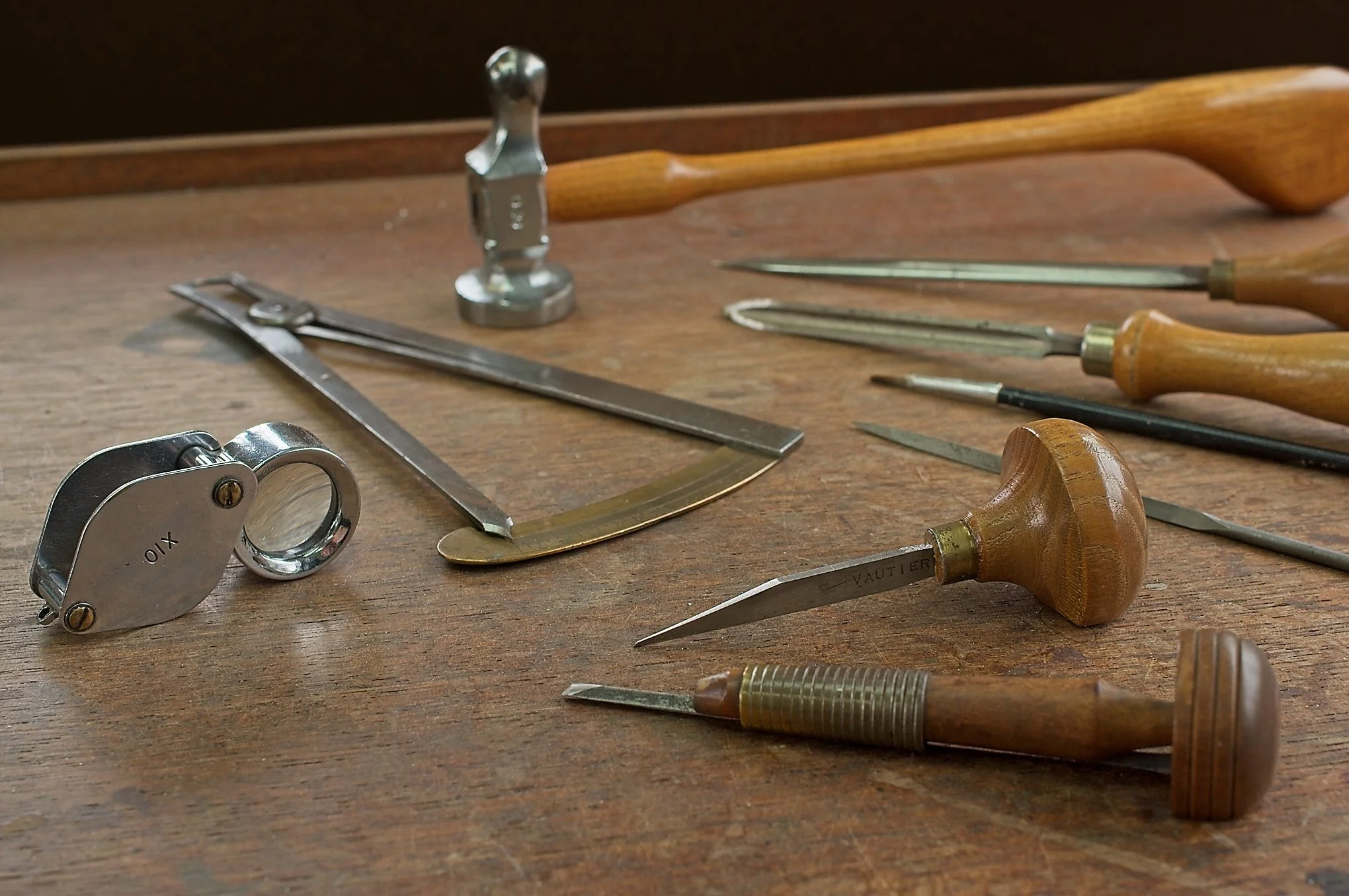 Woodworking tools on a workbench, including chisels, a saw, a hammer, and a marking gauge.
