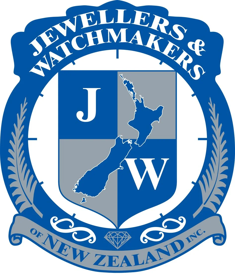 Logo for Jewelers & Watchmakers of New Zealand Inc., featuring a shield with a map of New Zealand divided into blue and gray sections, with the letters J and W, surrounded by a blue laurel wreath and a diamond symbol at the bottom.