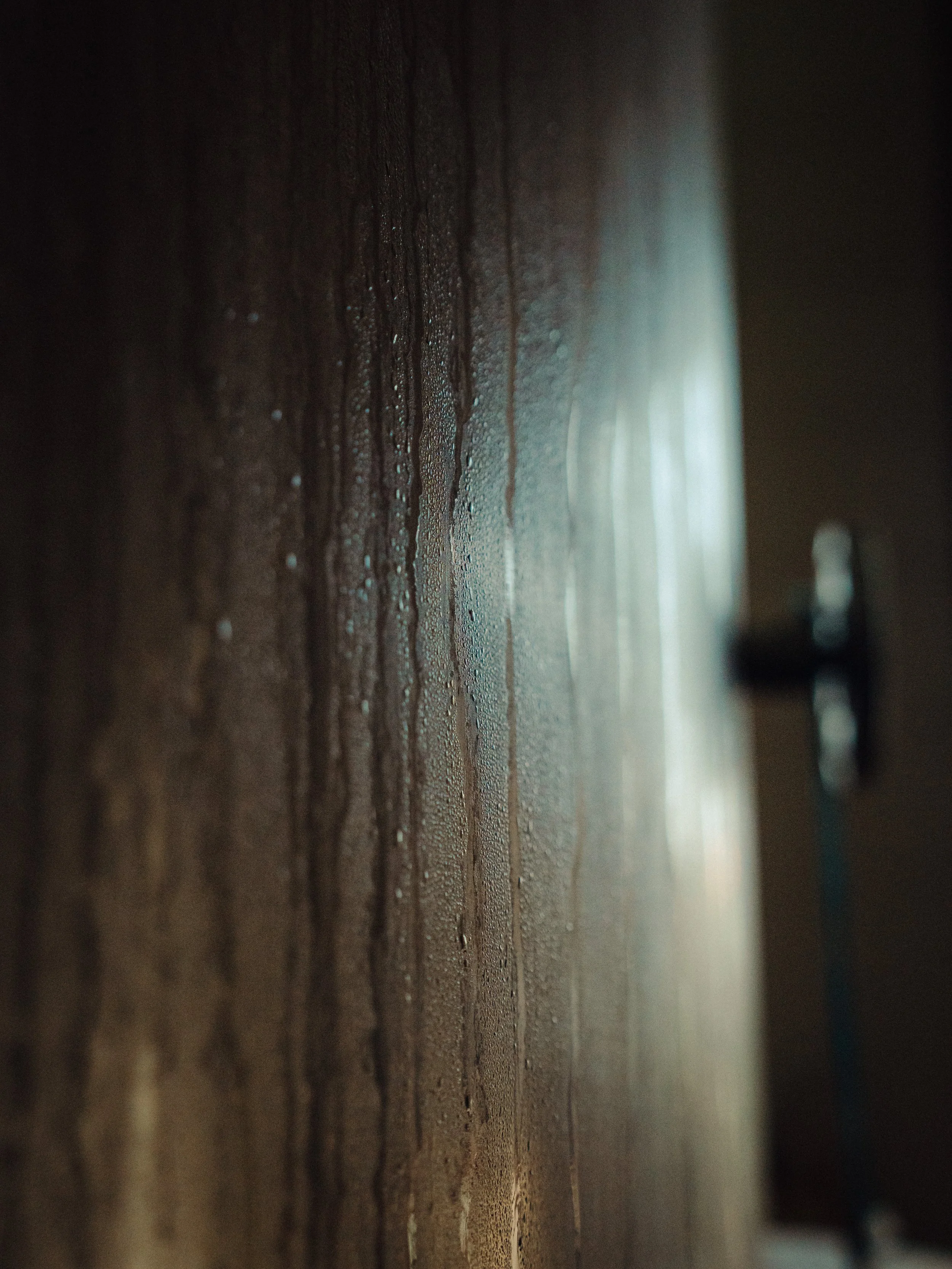 Une surface de mur en béton avec de la condensation et de l'eau qui s'écoule, éclairée par une lumière intense provenant d'une fenêtre ou d'une source lumineuse
