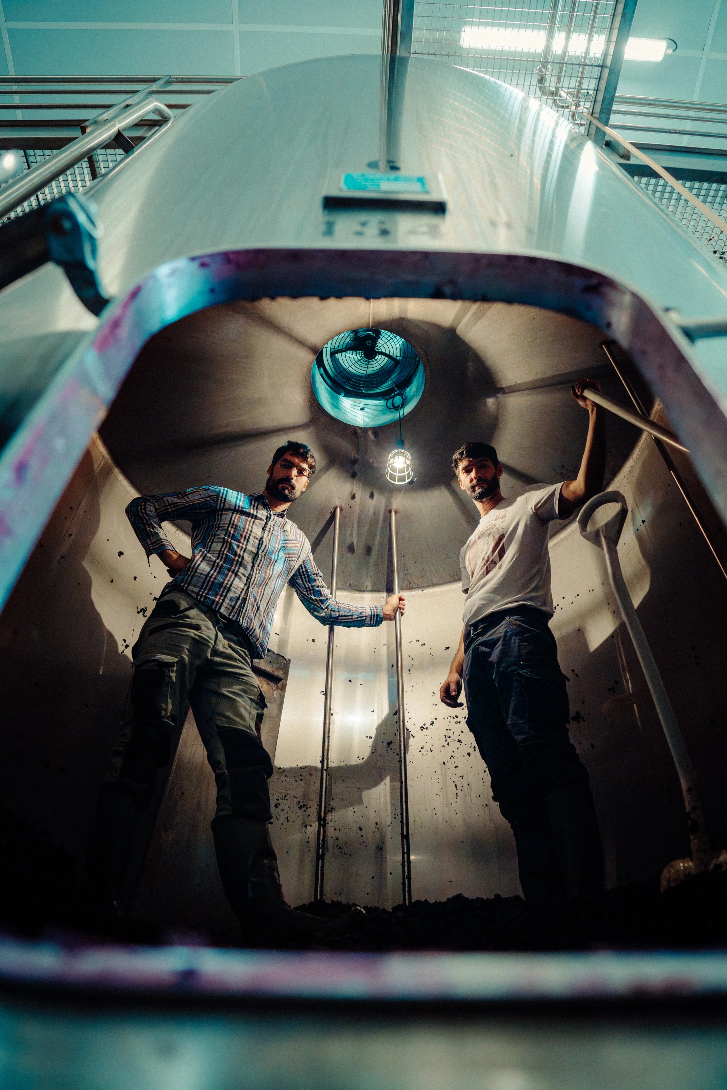 Deux hommes se tiennent à l'intérieur d'une chambre de fermentation ou d'une cuve industrielle en acier inoxydable, vue de l'intérieur de la cuve avec un point de vue en contre-plongée.
