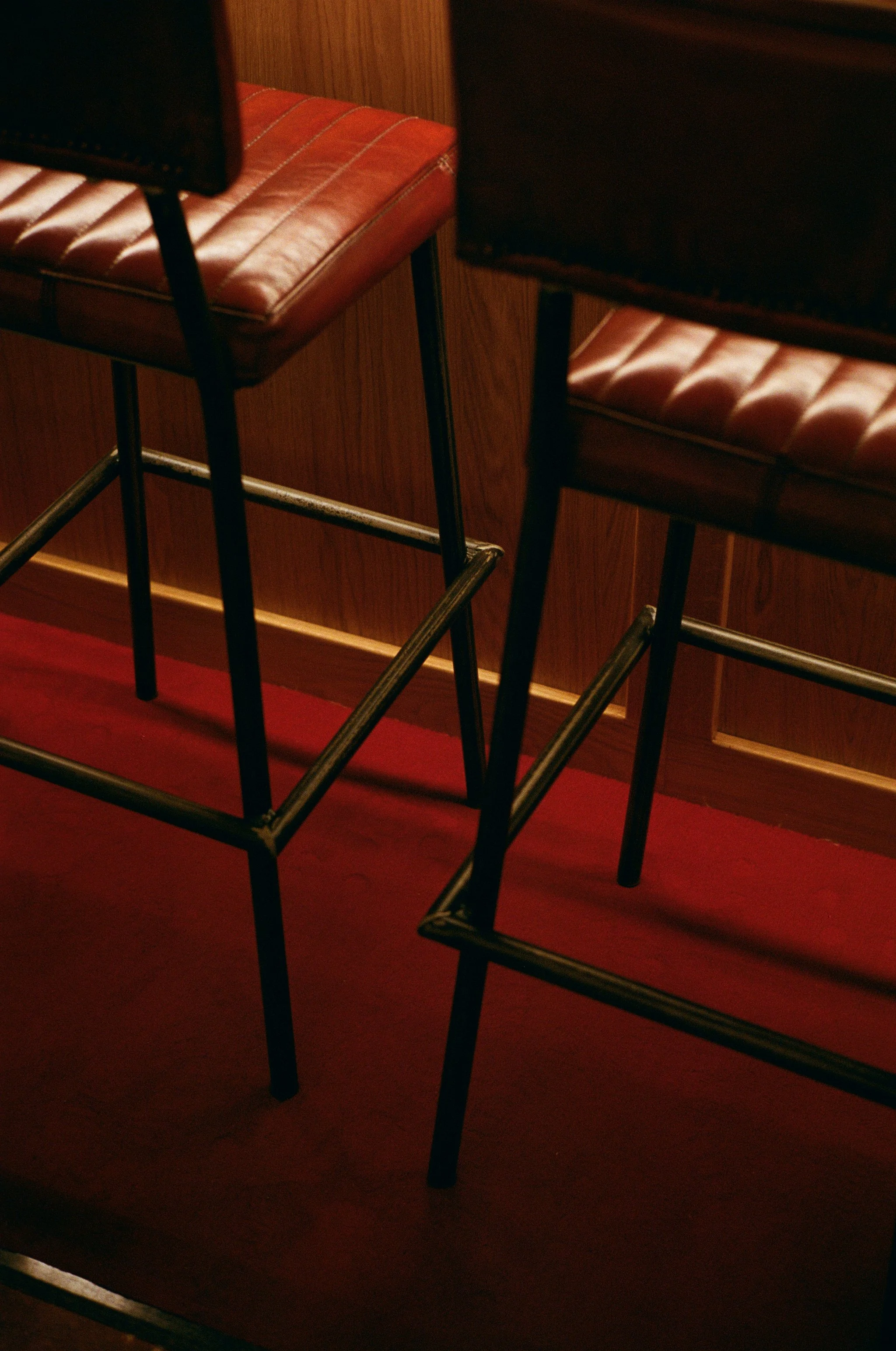 Deux tabourets avec des sièges en cuir marron et des pieds en métal, positionnés devant une armoire en bois.