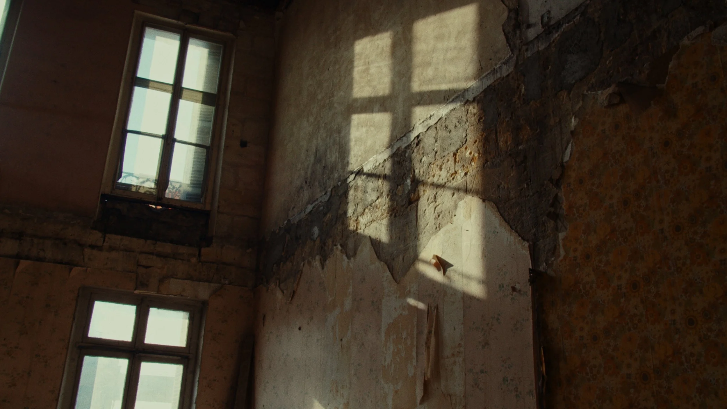 Intérieur d'une pièce ancienne avec murs endommagés et fenêtres éclaire par la lumière naturelle.