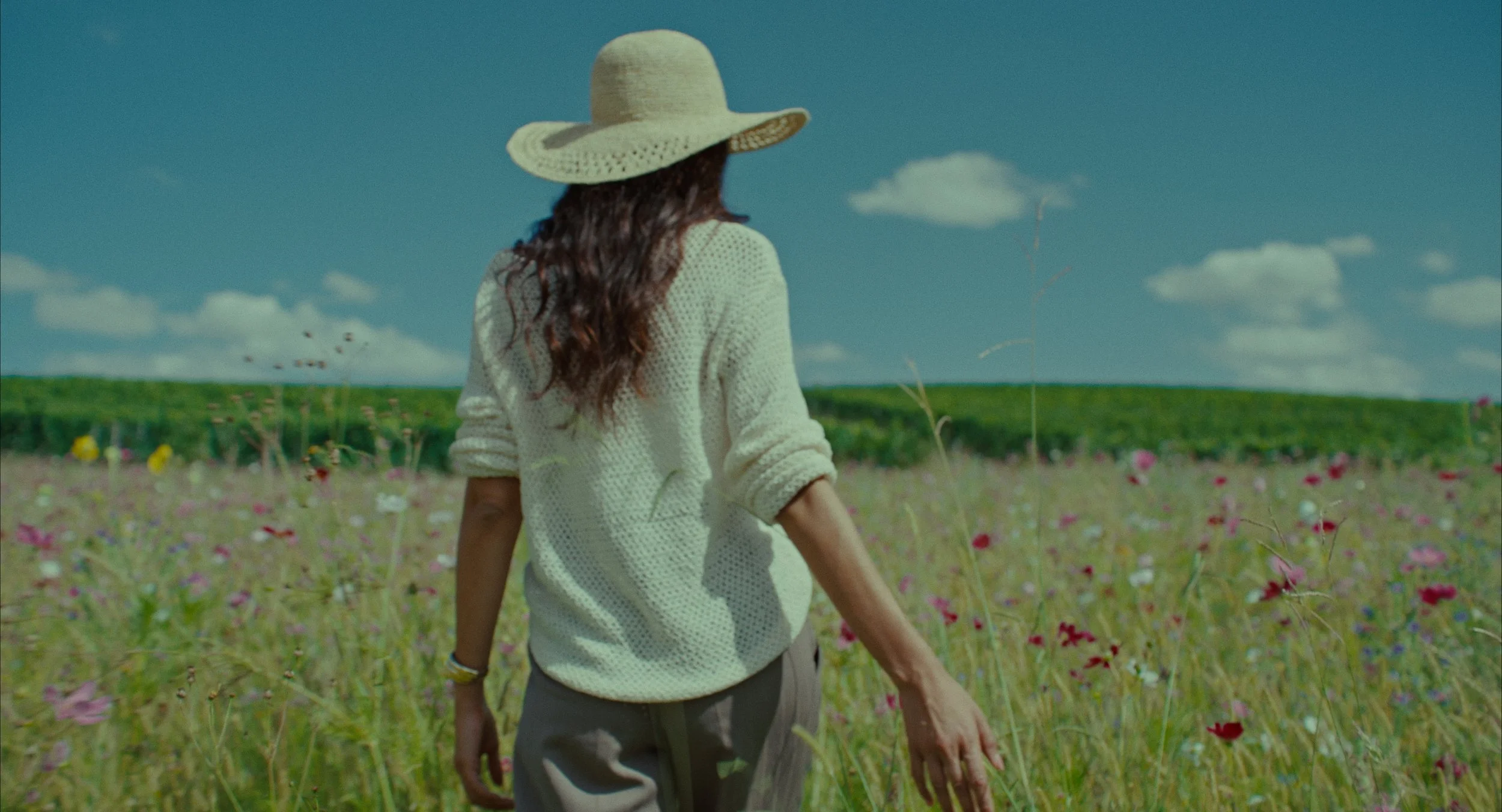 Une femme portant un chapeau de soleil et un pull blanc marche dans un champ de fleurs au printemps.