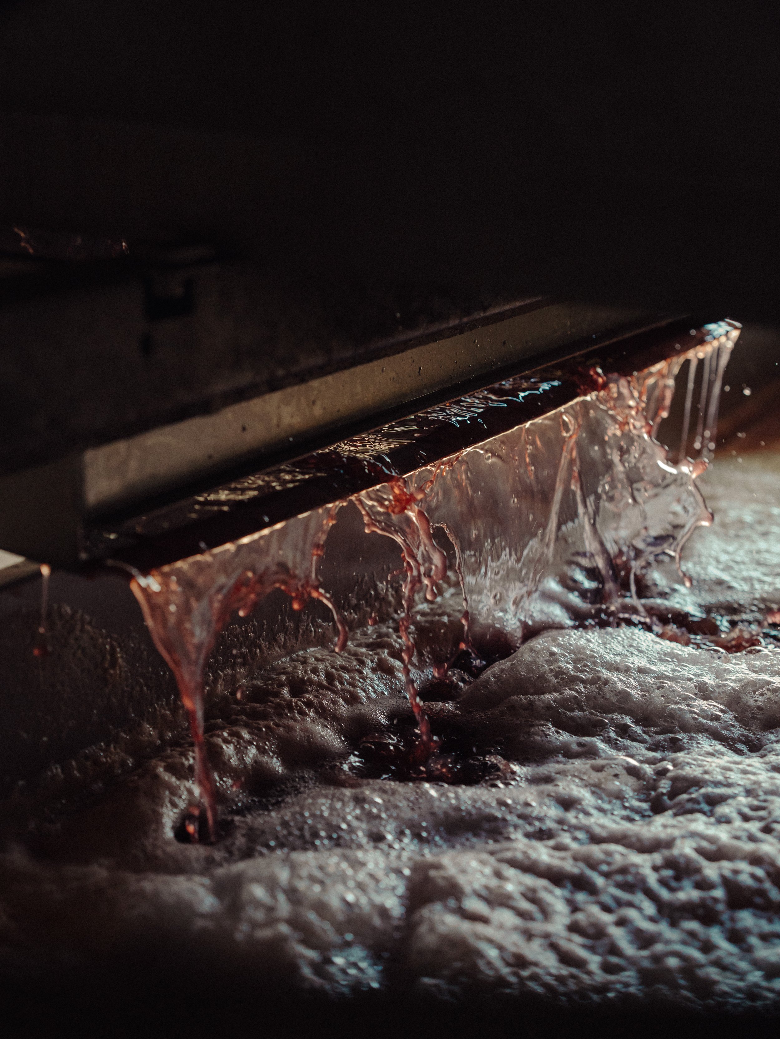 Le liquide rouge foncé coule d'une machine, formant des bulles et des gouttelettes sur une surface noire.
