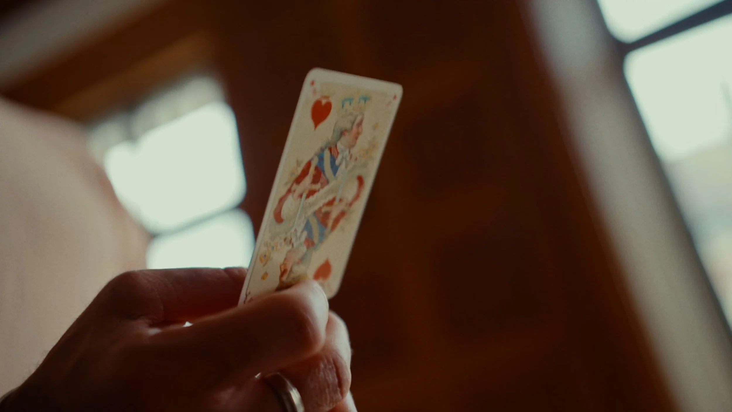 Main tenant une carte à jouer de la Reine de cœur, prise en gros plan.