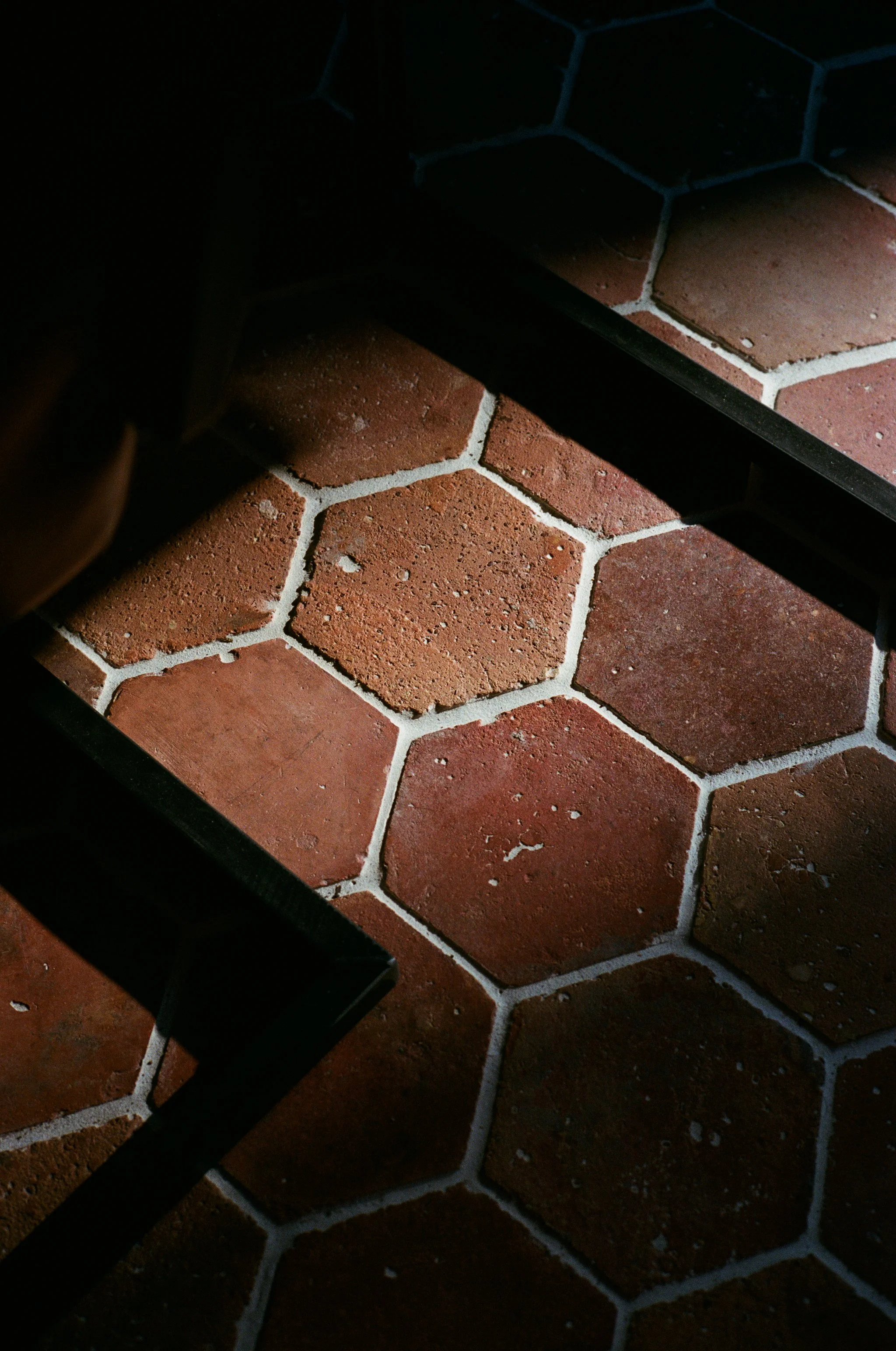 Sol en carreaux de céramique hexagonaux rouges foncés, avec des joints blancs, vue partiellement ombragée.