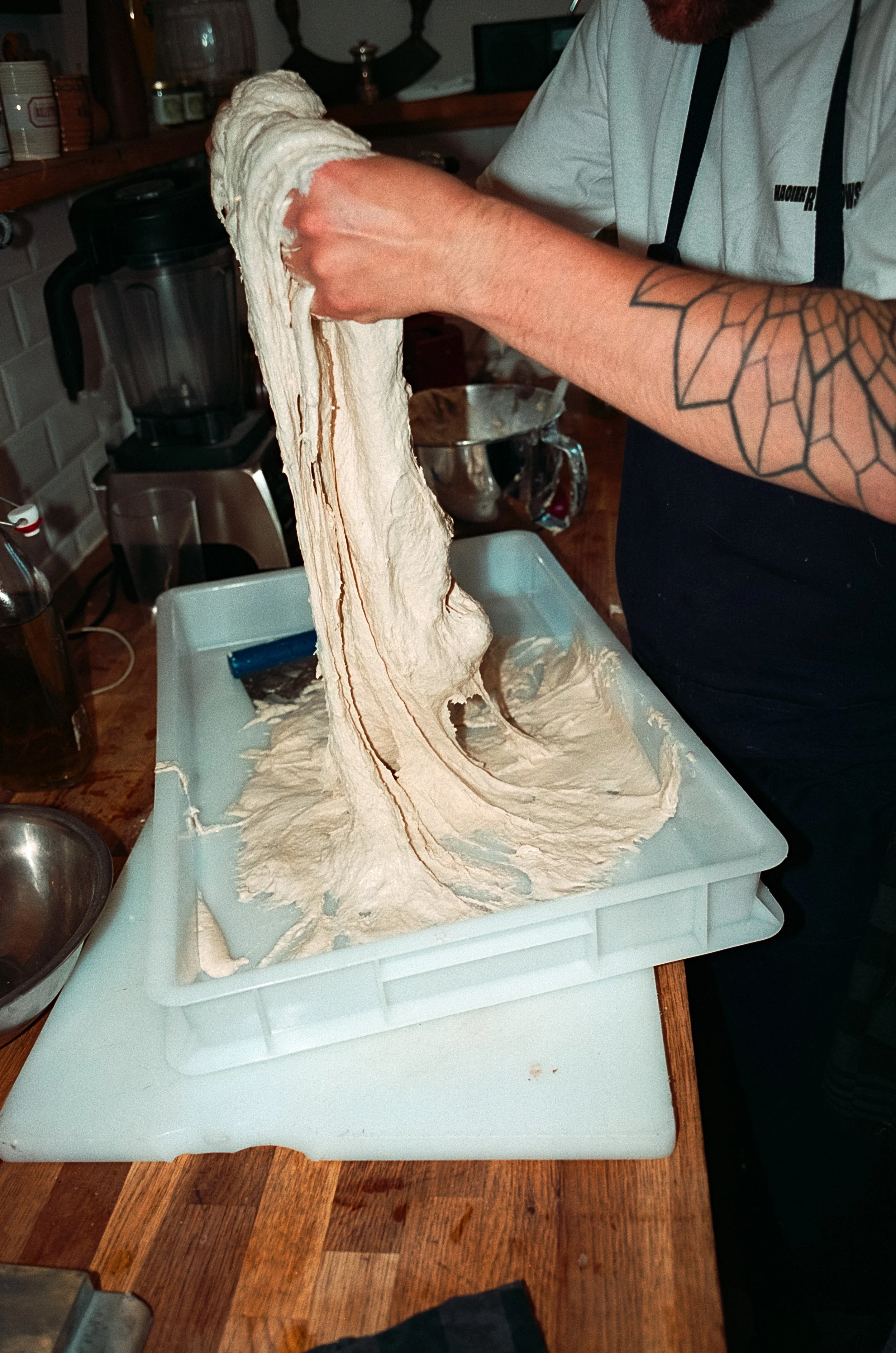 Une personne en train de faire de la pâte à levure qui s'étire sur une surface en plastique, dans une cuisine.
