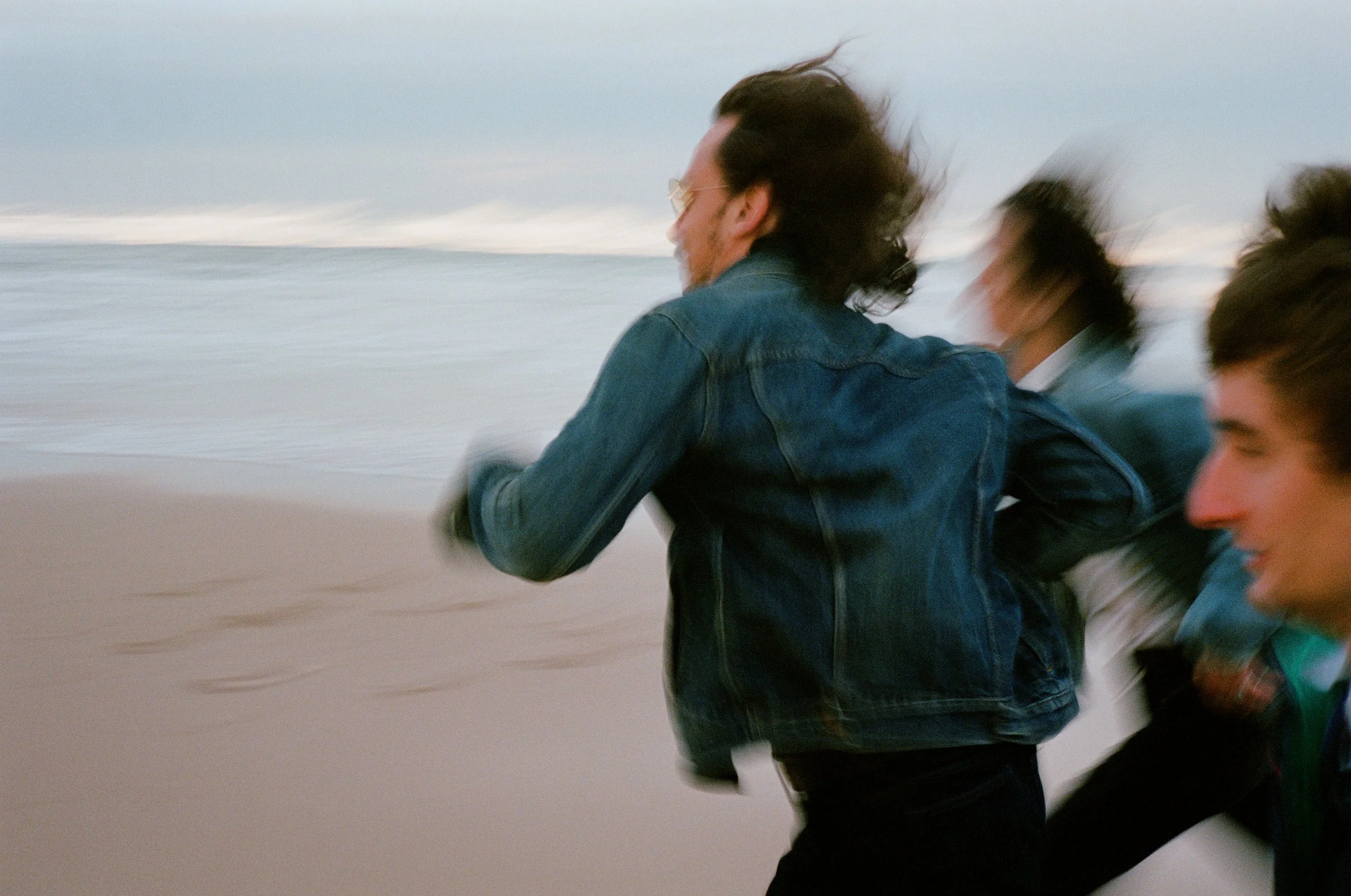 Trois jeunes gens courant sur la plage, avec la mer en arrière-plan, en train de profiter d'une promenade ou d'une course dans le vent.