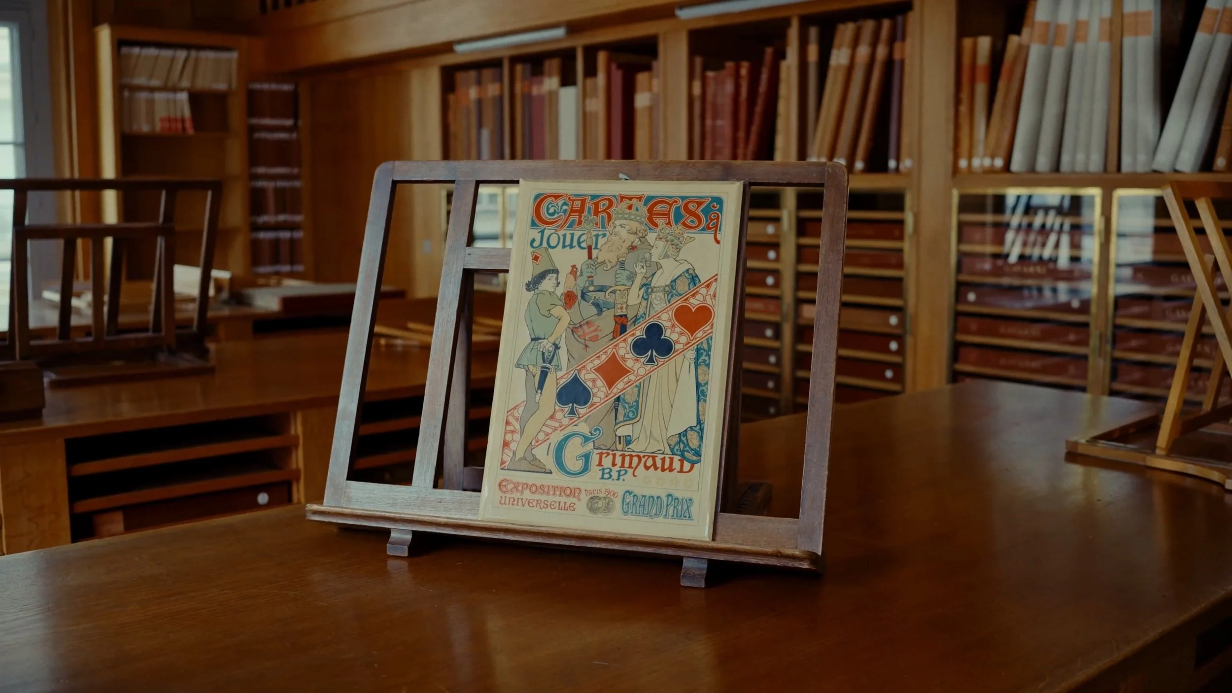 Une vieille affiche de jeu de cartes dans un cadre en bois sur une table en bois, avec des étagères remplies de livres en arrière-plan.