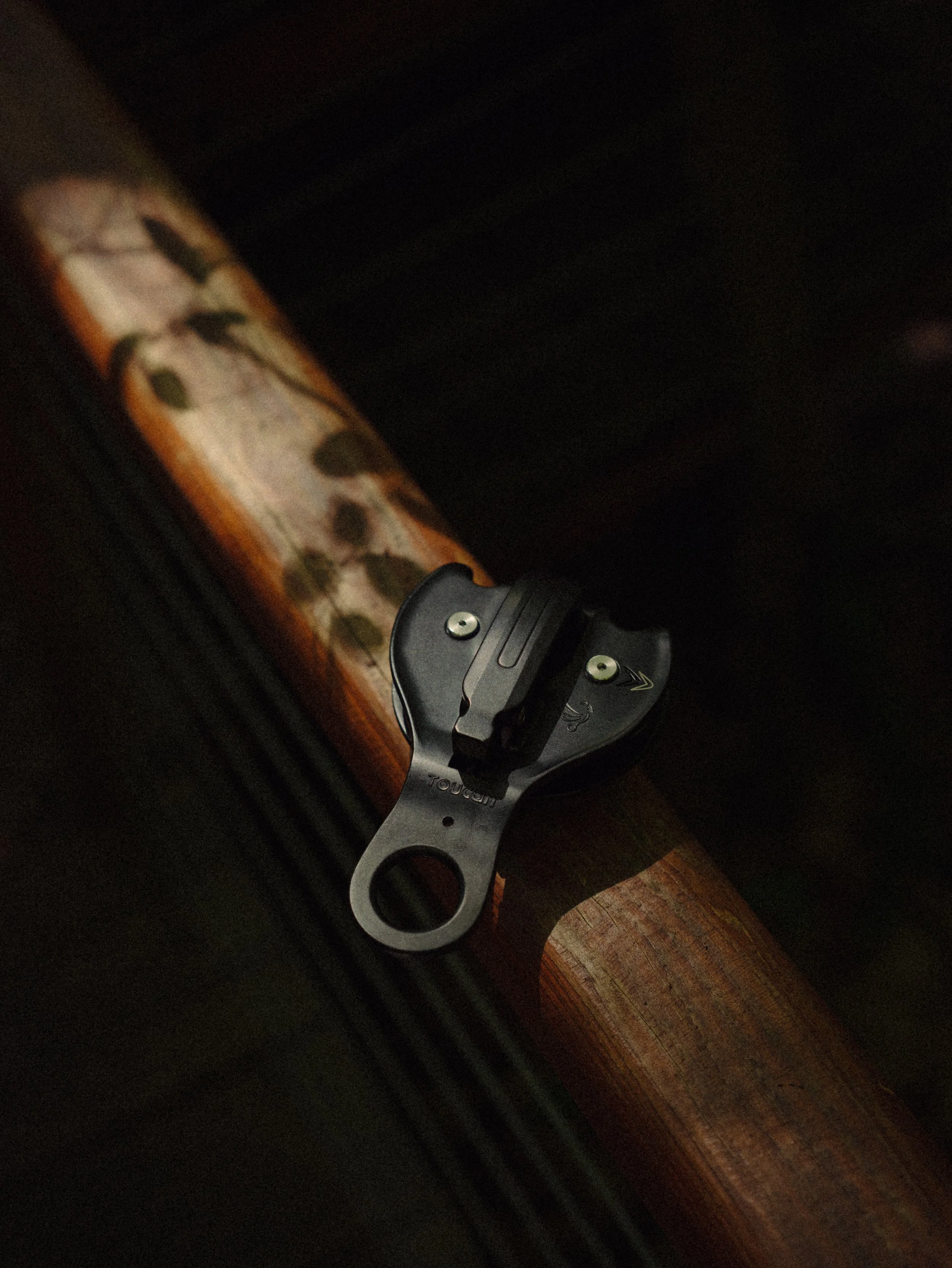 Fusil avec mécanisme de déclenchement visible, posé sur une surface sombre. Le bois du fusil présente des motifs en forme de feuilles ou de pois.