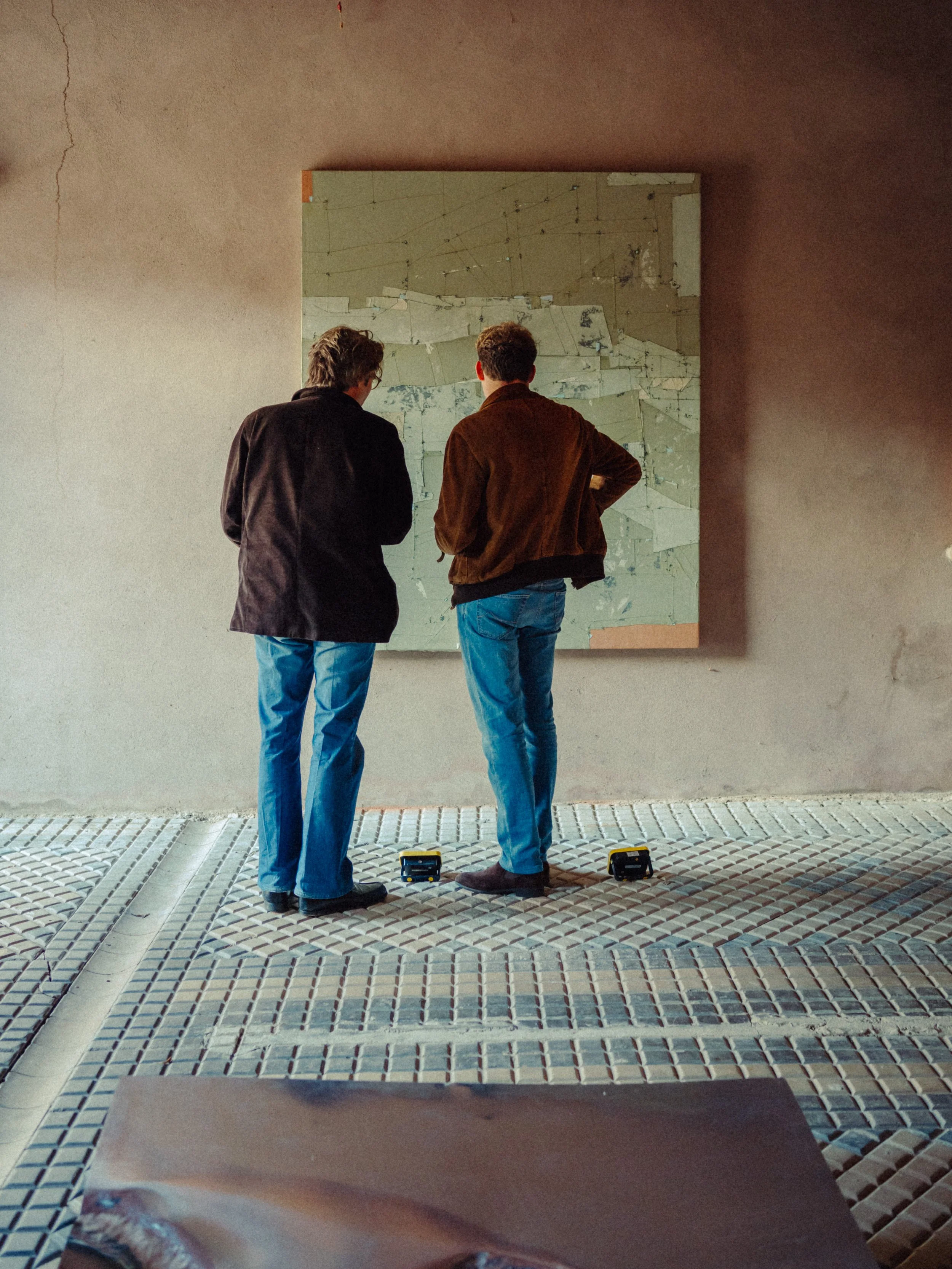 Deux hommes debout devant une œuvre d'art abstraite dans un espace d'exposition, vu de dos.