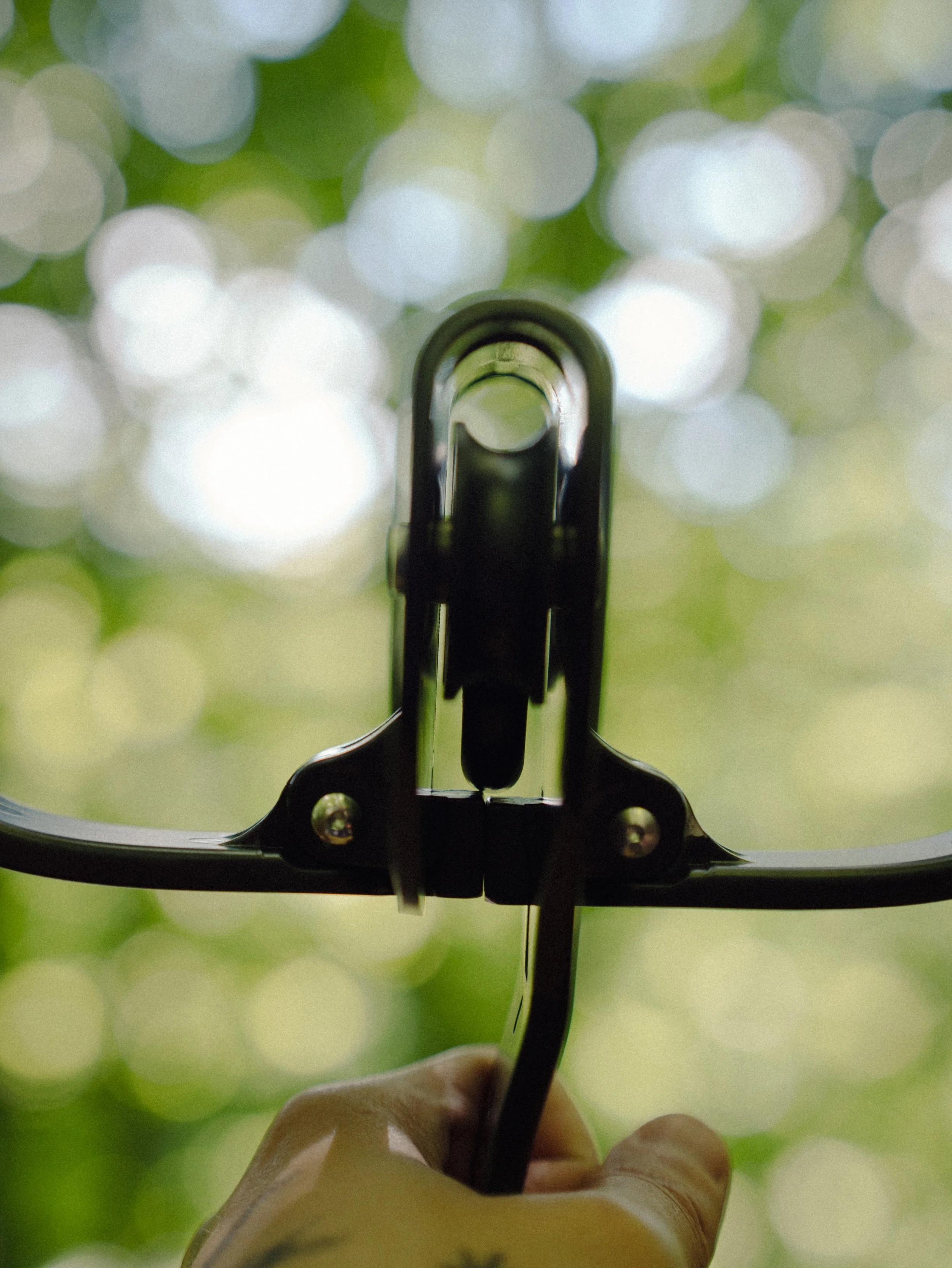Une personne tient une courroie de tir à l'arc, pointée vers le haut, avec un fond flou de feuillage vert et de lumière.