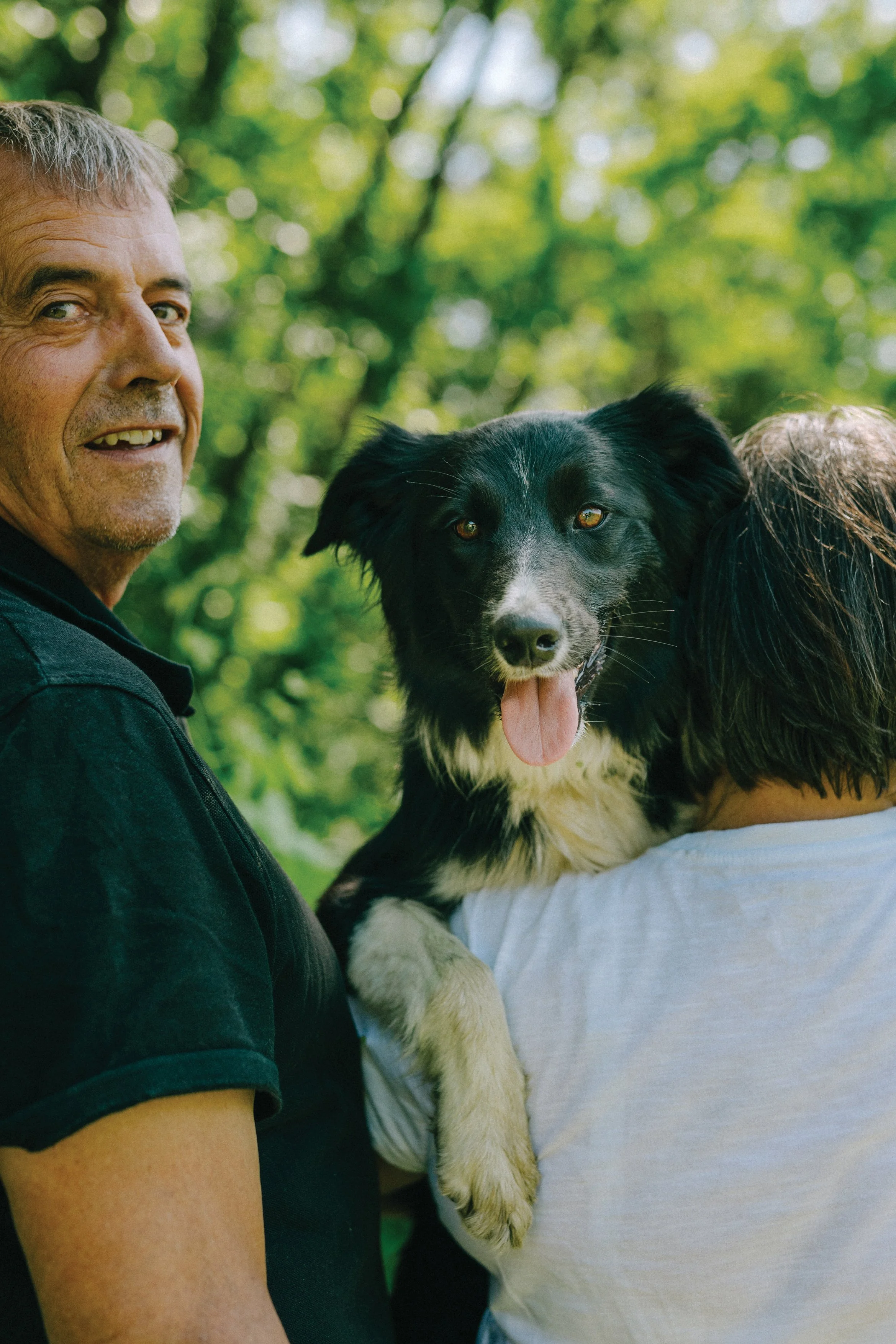 Un homme et une femme tiennent un chien noir et blanc dans un parc verdoyant.