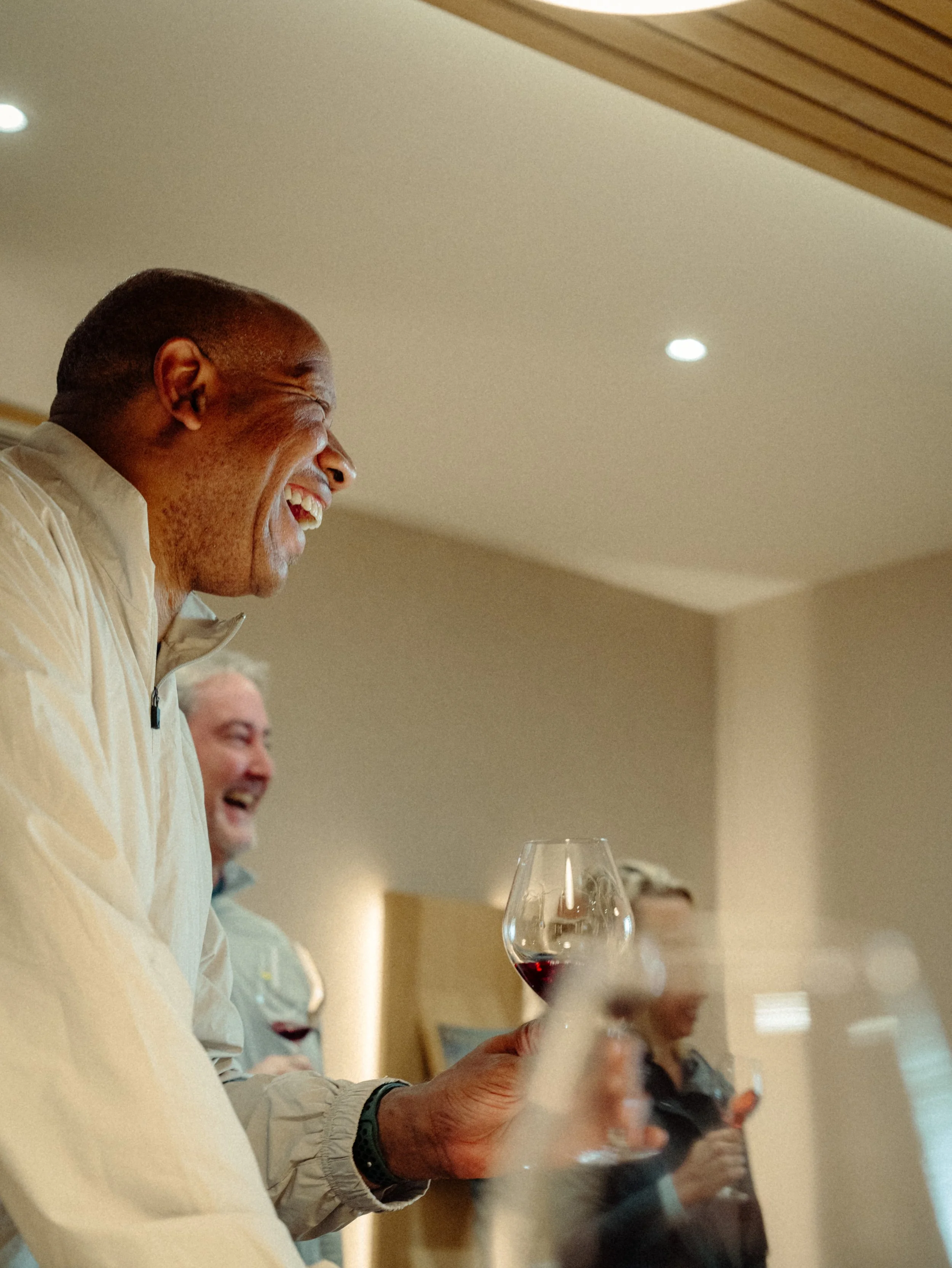 Groupe de personnes souriantes tenant un verre de vin rouge dans un intérieur lumineux.
