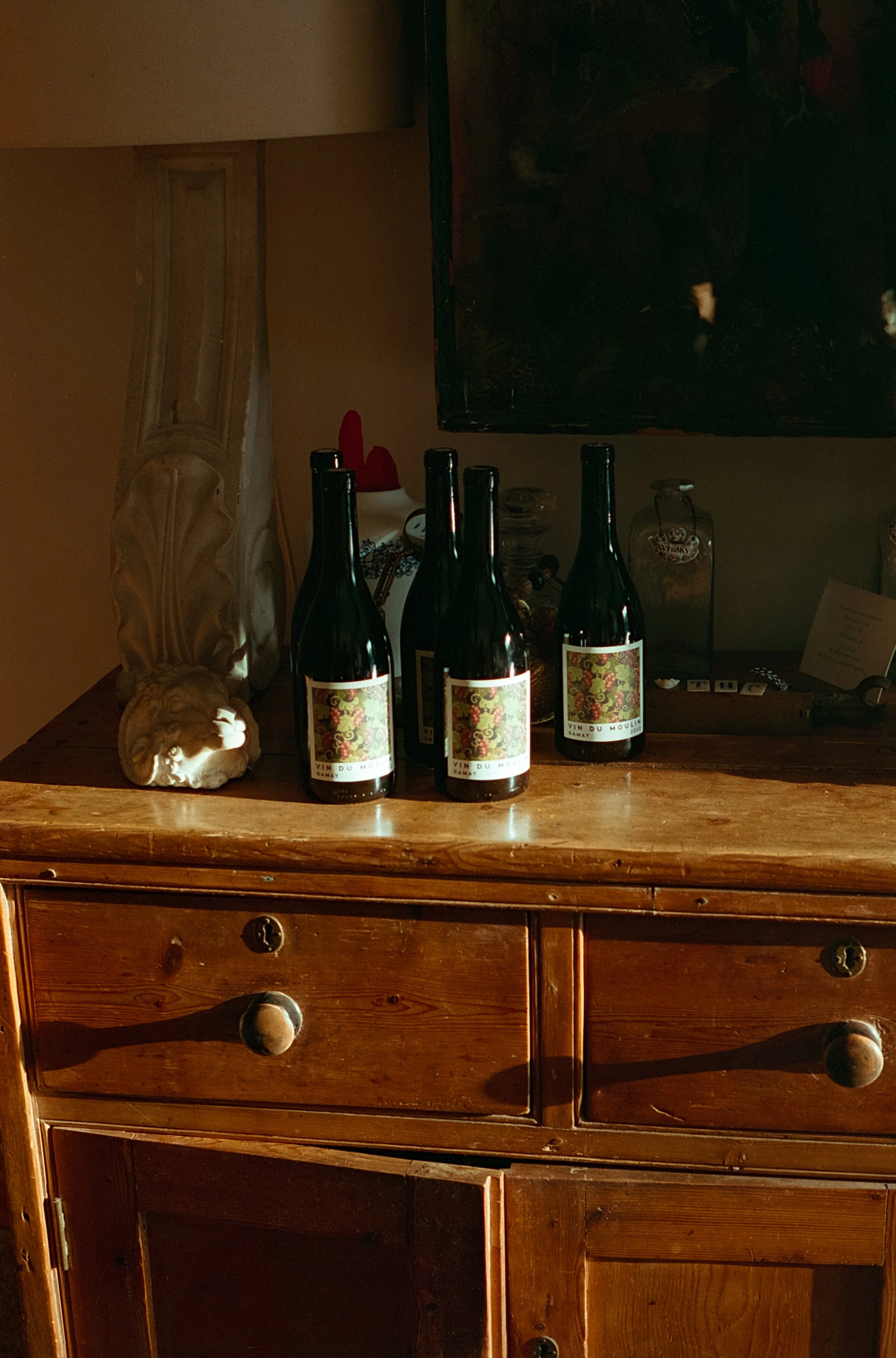 Quatre bouteilles de vin rouge sur une vieille commode en bois dans une pièce sombre.