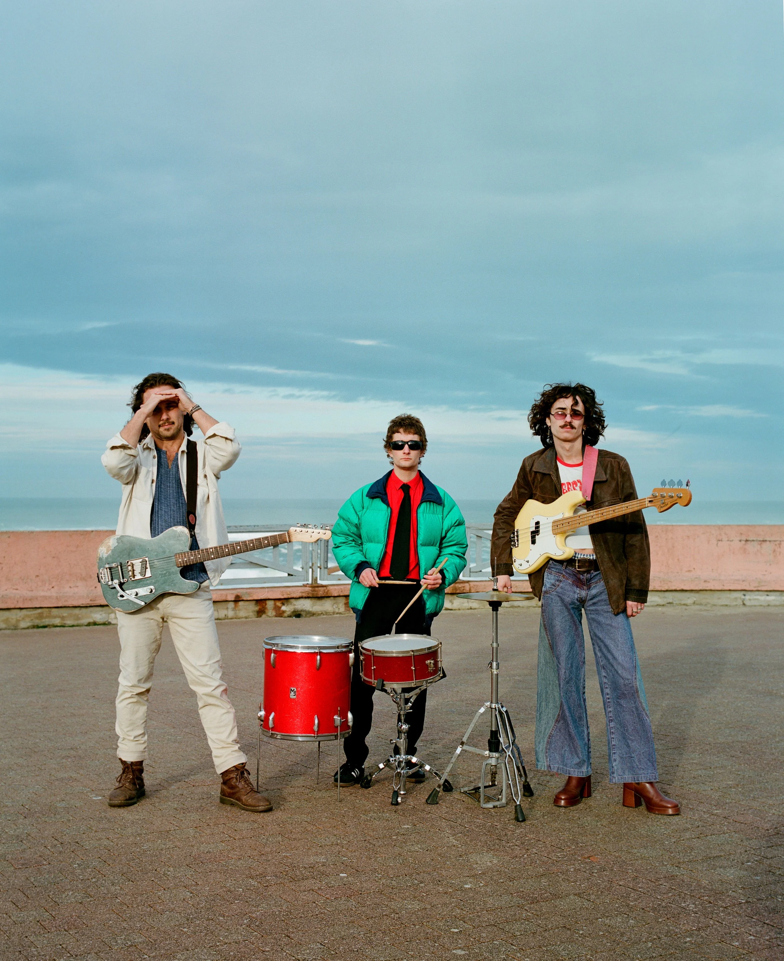 Un groupe de trois musiciens avec leurs instruments sur une promenade en plein air, sous un ciel nuageux.